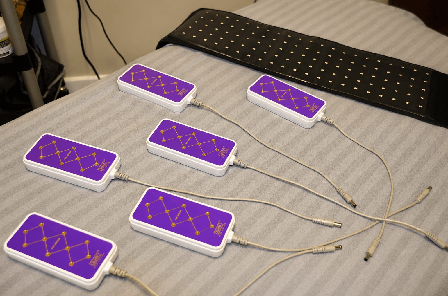 Six purple electronic devices with yellow lines connected by wires on a bed, with a black case nearby.