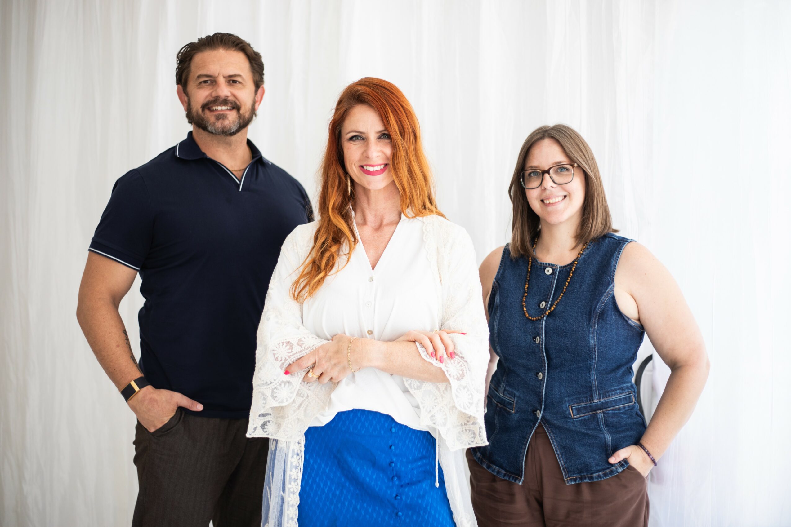 Three people standing together, smiling, in front of a white curtain background.