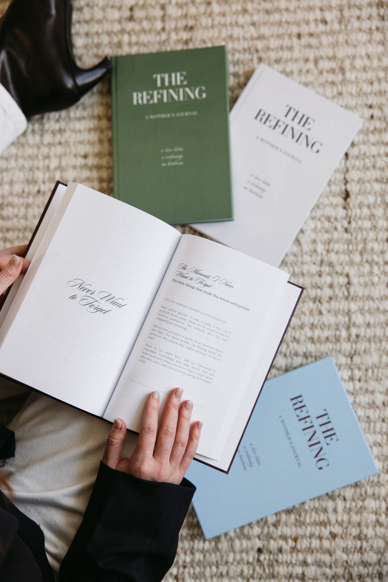 Person holding open book with text, surrounded by three other books titled 'The Refining' in green, white, and blue covers, on a textured surface.