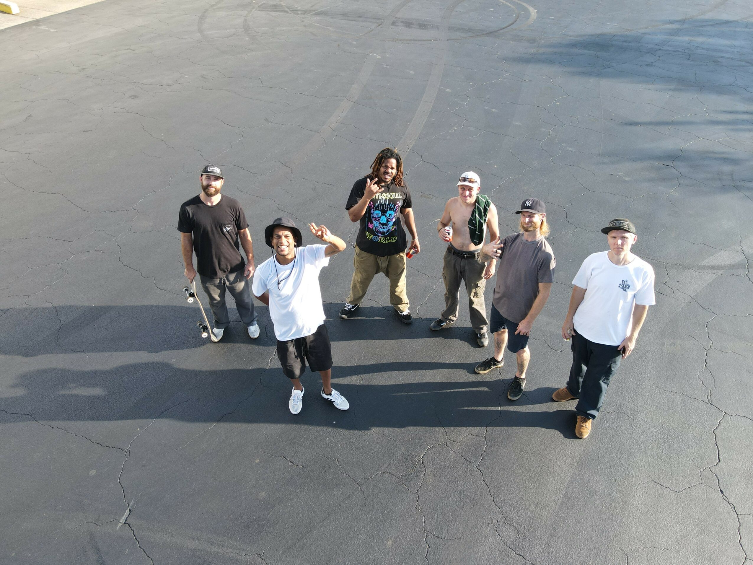 Six people standing on a paved surface, some wearing hats and sunglasses, with shadows cast on the ground.