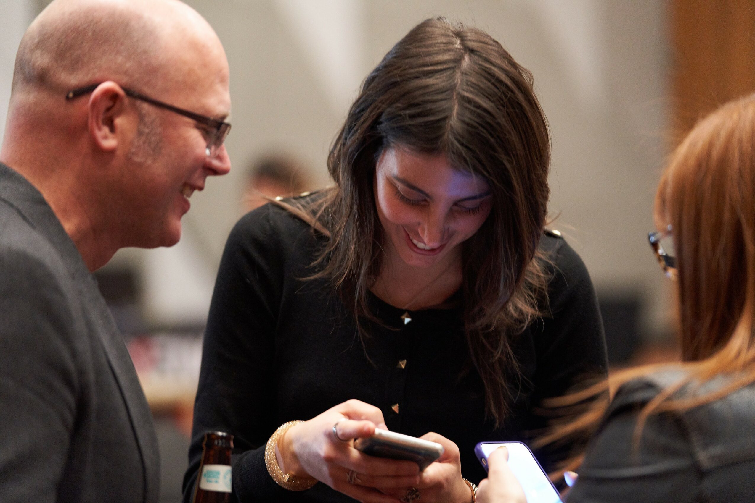 Three people smiling and looking at a phone together in an indoor setting.