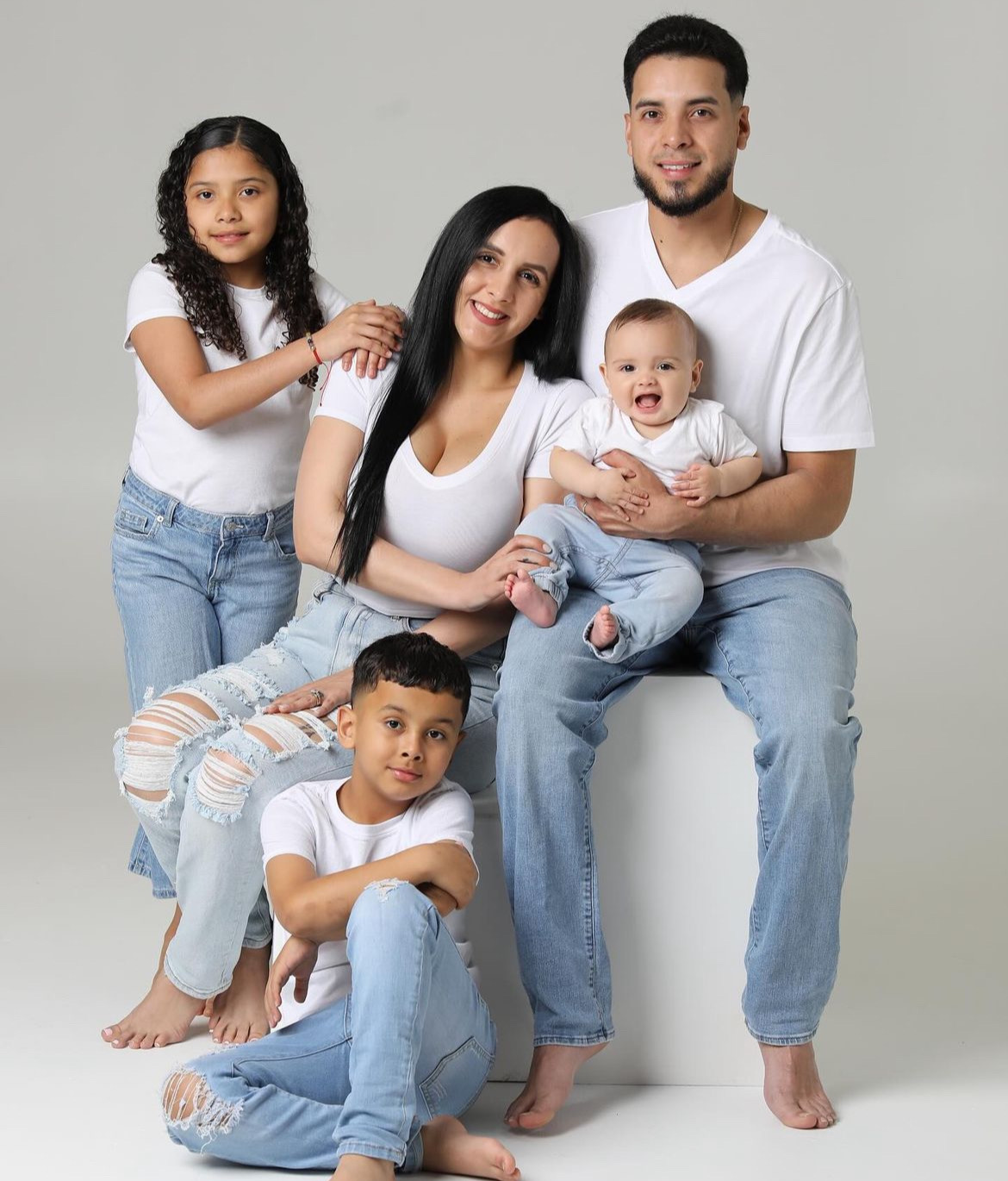 Family of five with two children, smiling and sitting together against a plain background.
