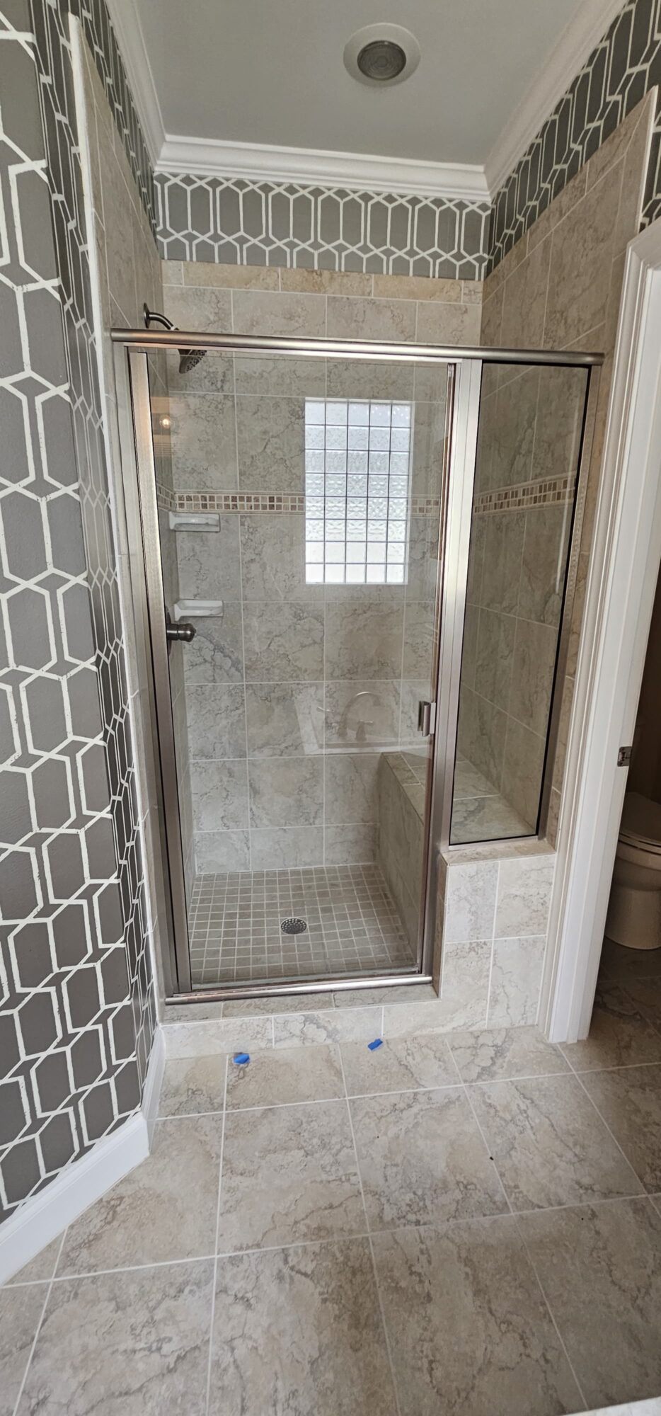 Small bathroom shower with glass door, tiled walls, and a window inside, viewed from the doorway.