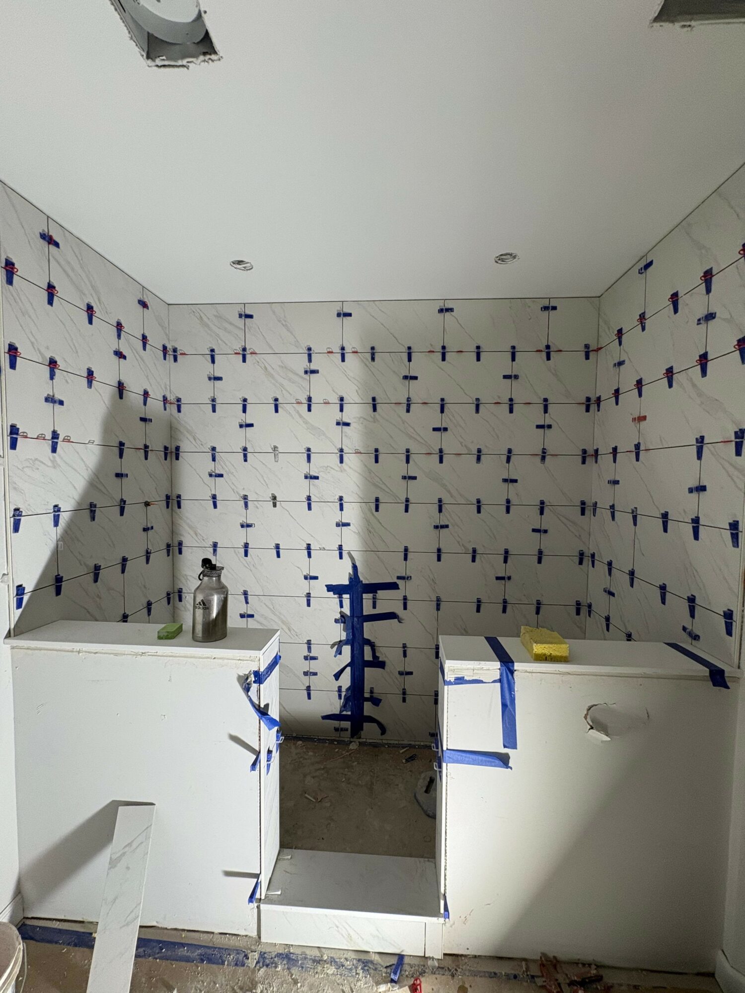 Bathroom with tiled walls, two sinks, and a blue faucet, under construction or renovation.