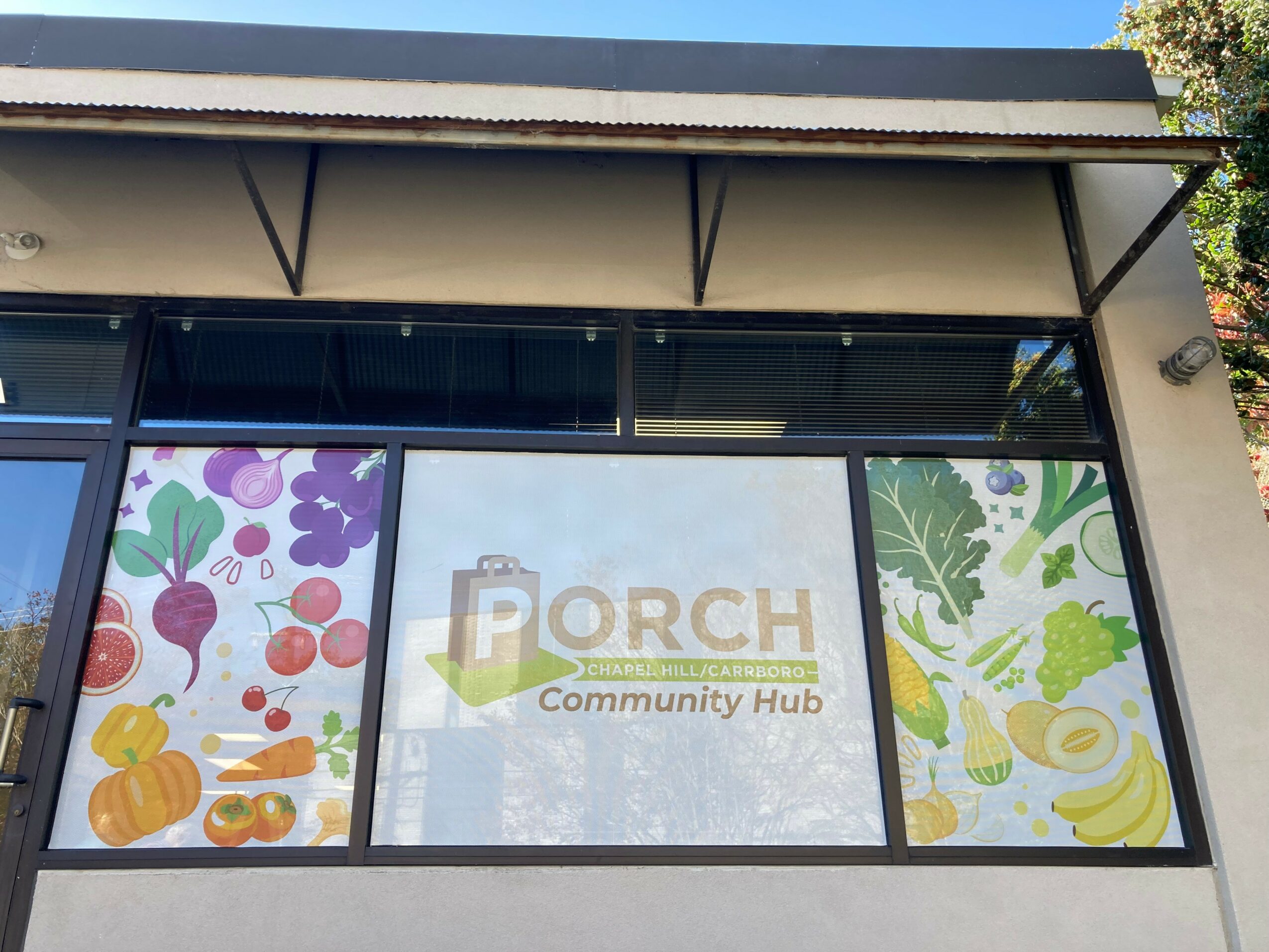 Community hub sign with colorful vegetables and the word 'Porch' in the center, viewed through a window.