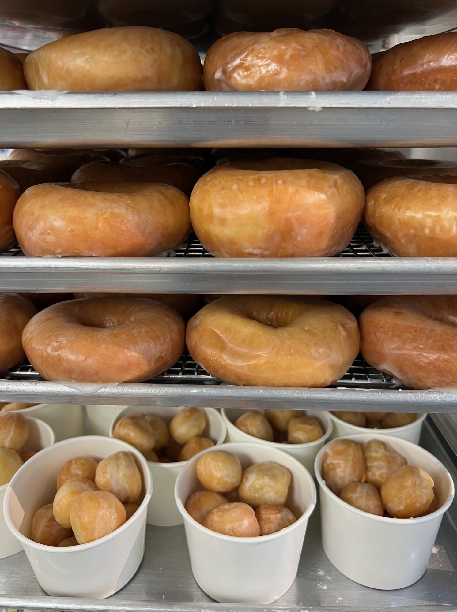 Rows of glazed donuts and cups filled with small round snacks on a tray.