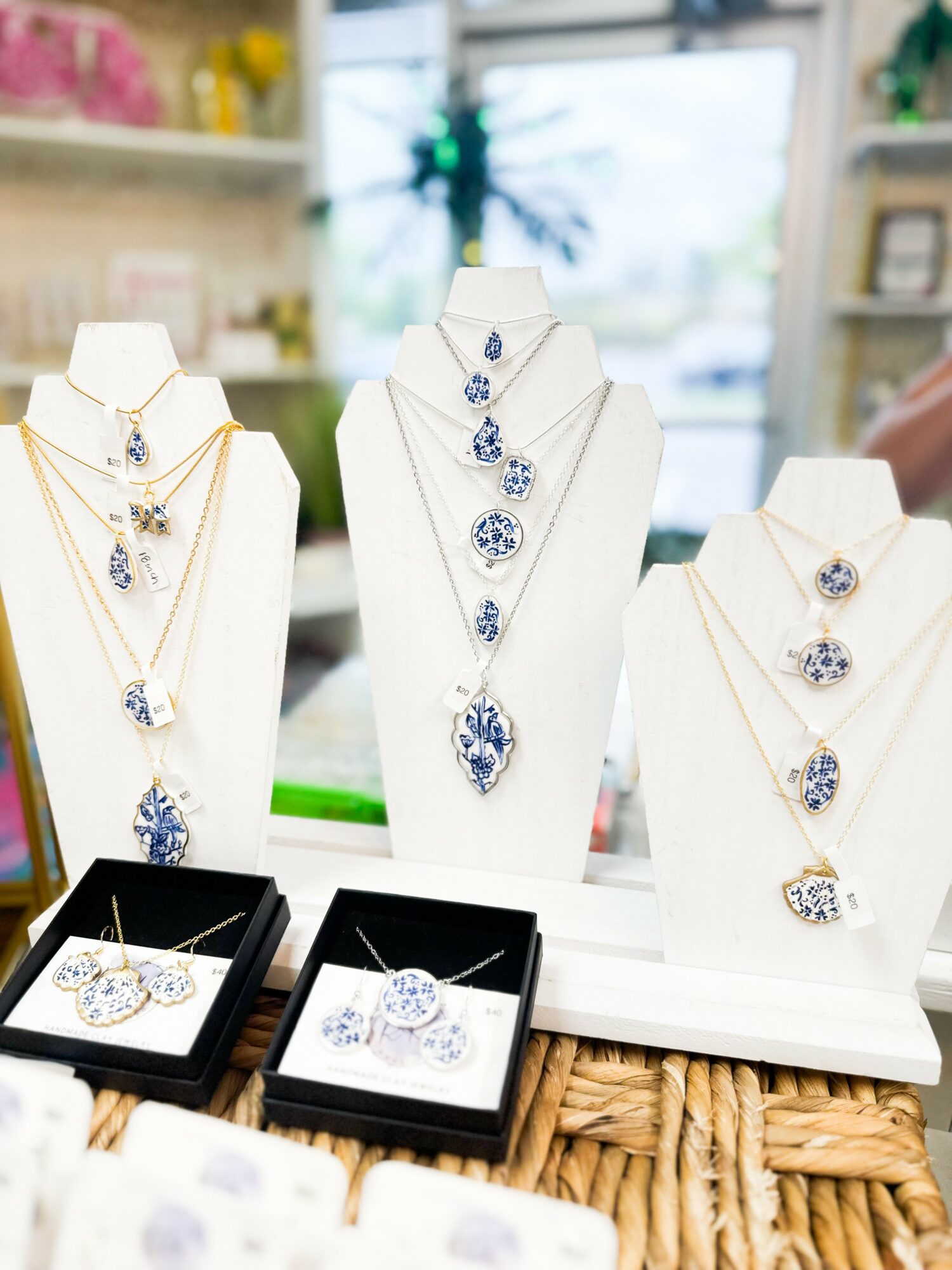Display of jewelry necklaces and earrings with blue and clear stones on white stands in a store, background blurred.