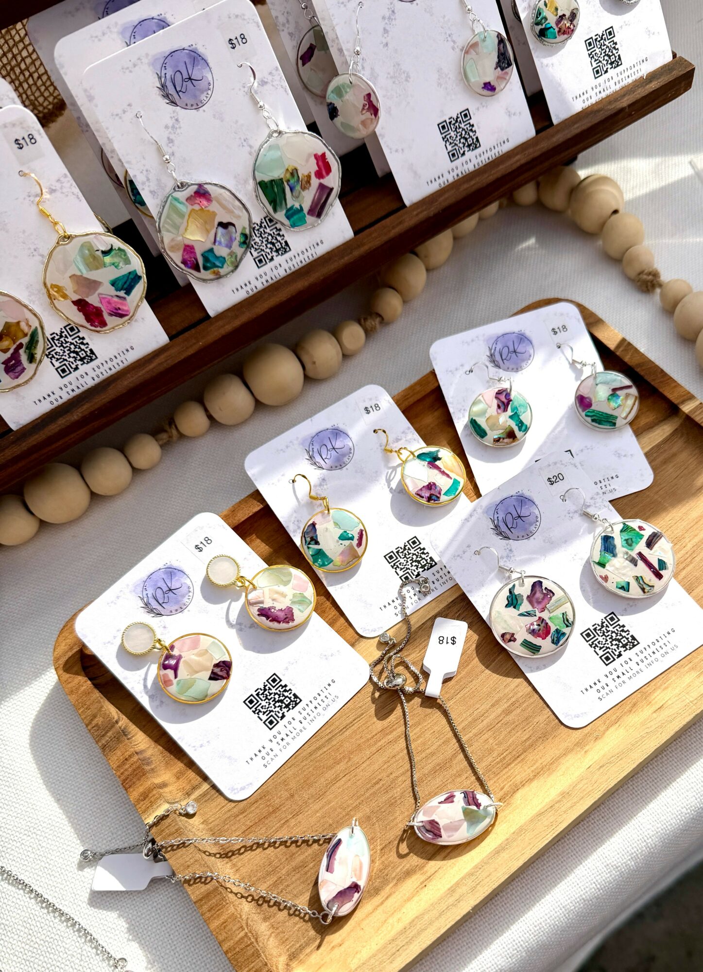 Display of colorful earrings and matching pendant on cards, arranged on a wooden tray with beads and a keychain, viewed from above.