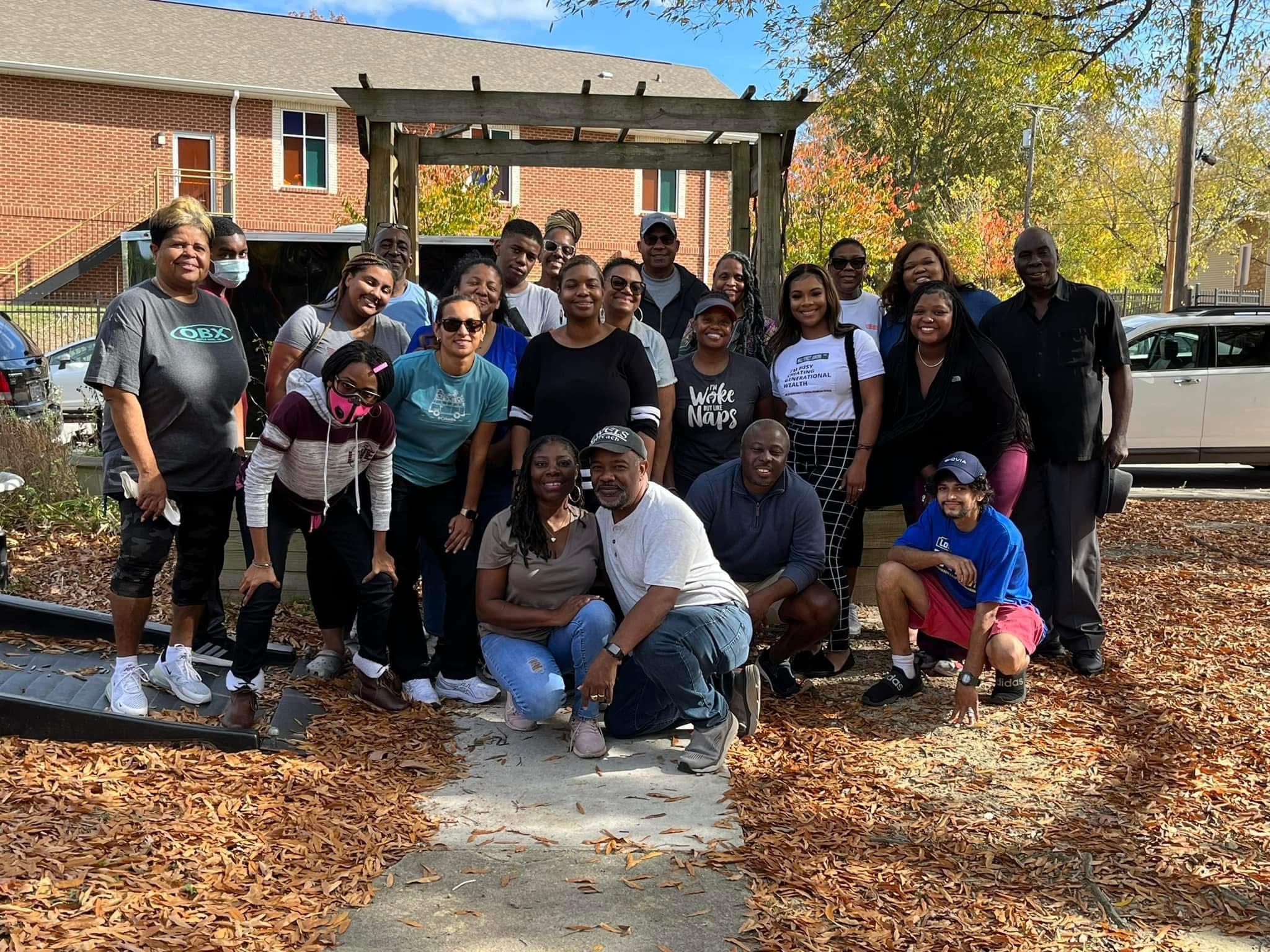 Group of people outdoors in fall, standing and kneeling on a path with trees and a building in background.