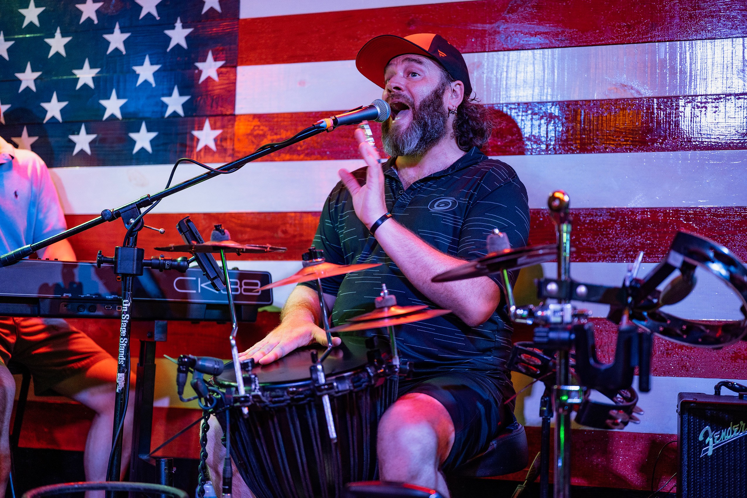 Person singing into microphone with musical instruments and American flag background.