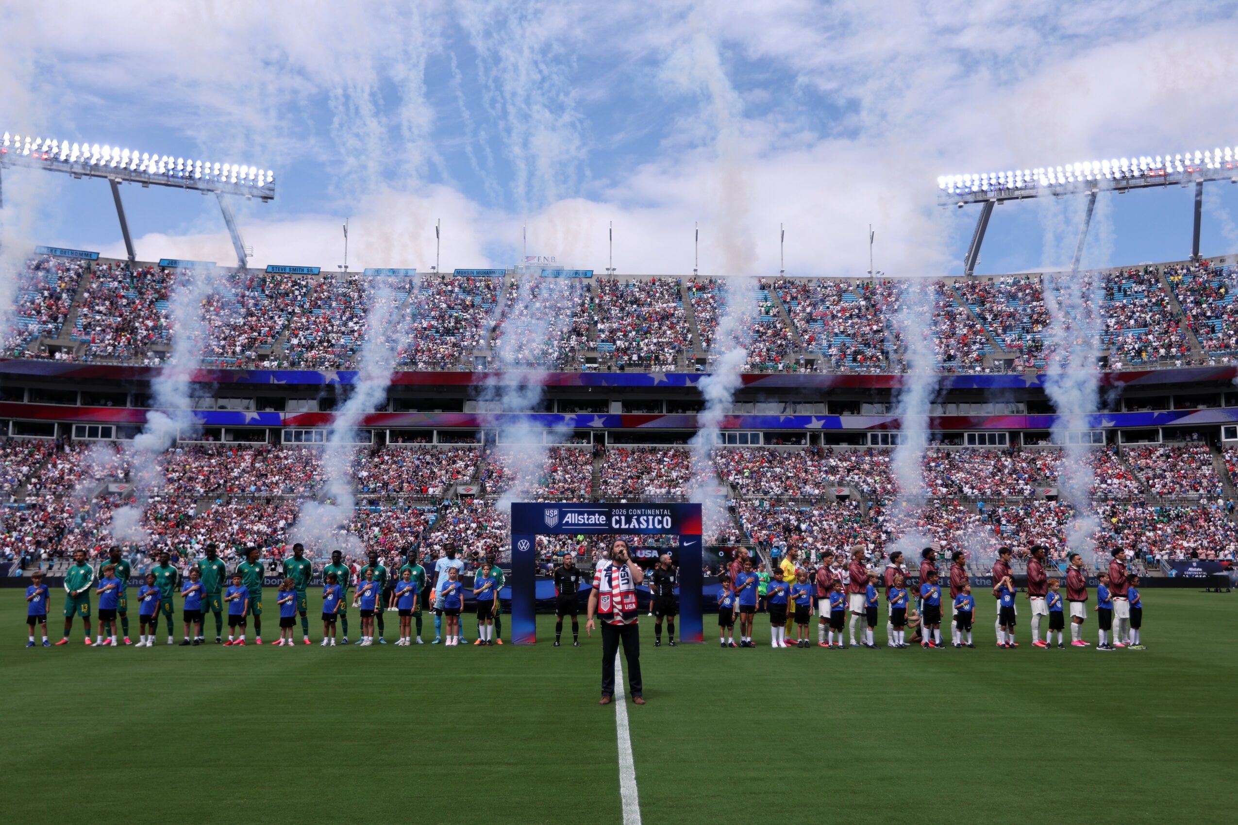 Crowd in stadium with fireworks and confetti, players on field, and a referee in the center, celebrating a sports event.
