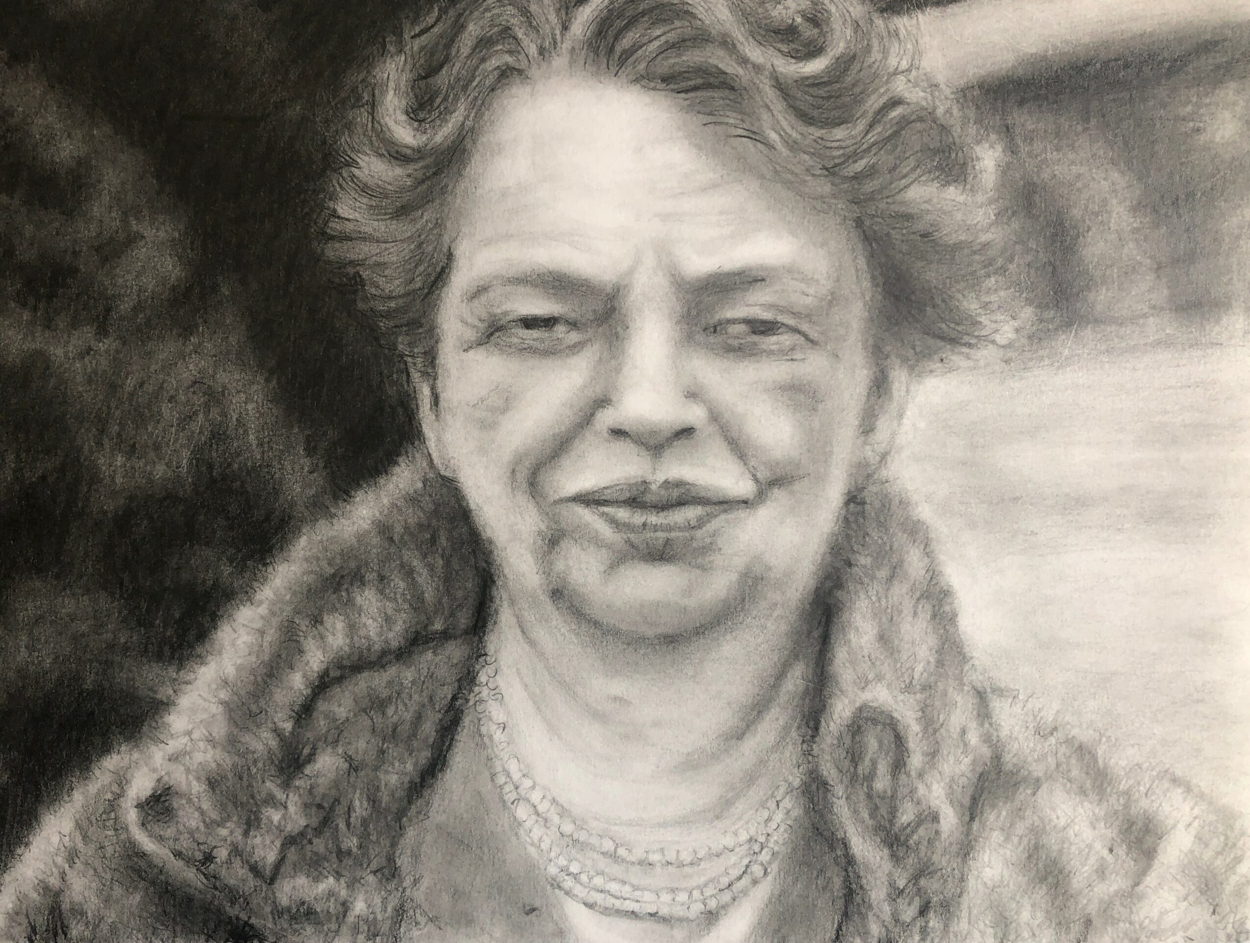 Woman with curly hair wearing a fur coat and layered necklaces, smiling slightly.