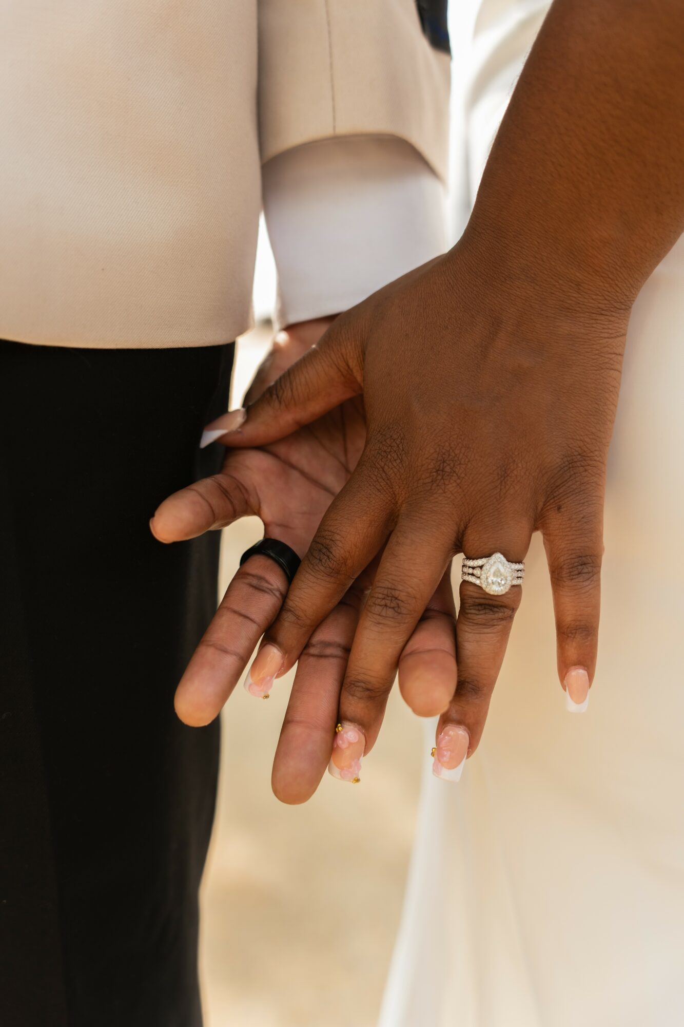 Two people hold hands, one with a ring on the ring finger, close-up of hands and fingers.