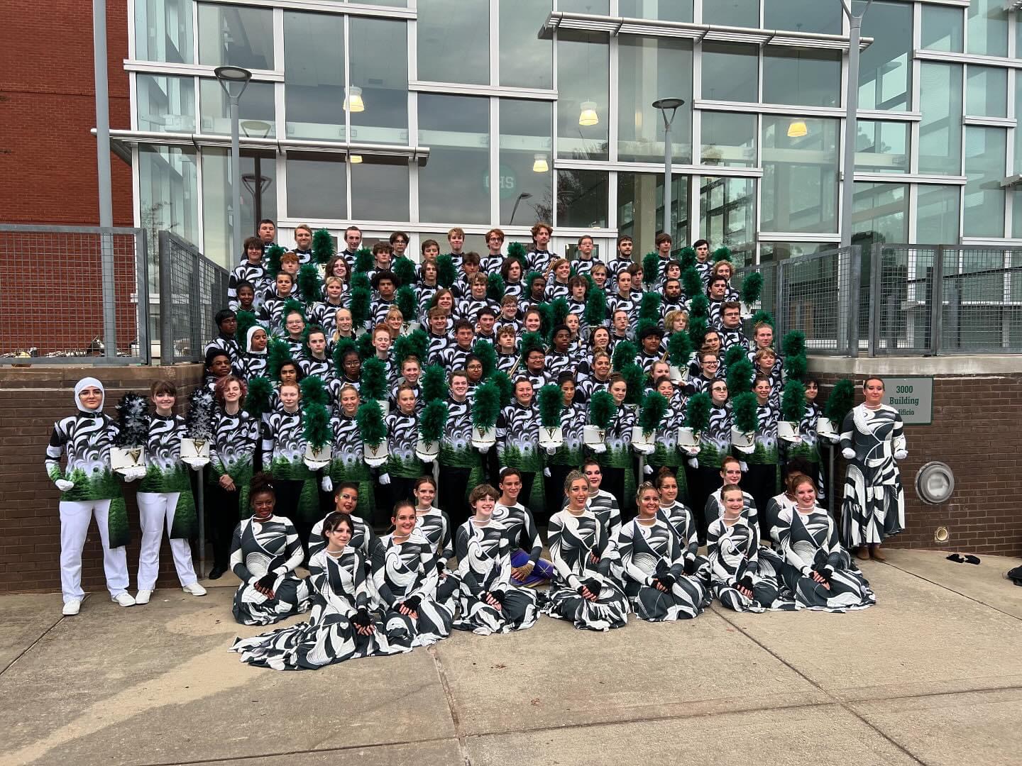 Large group of cheerleaders in uniform posing outside a modern glass building, arranged in rows on steps.
