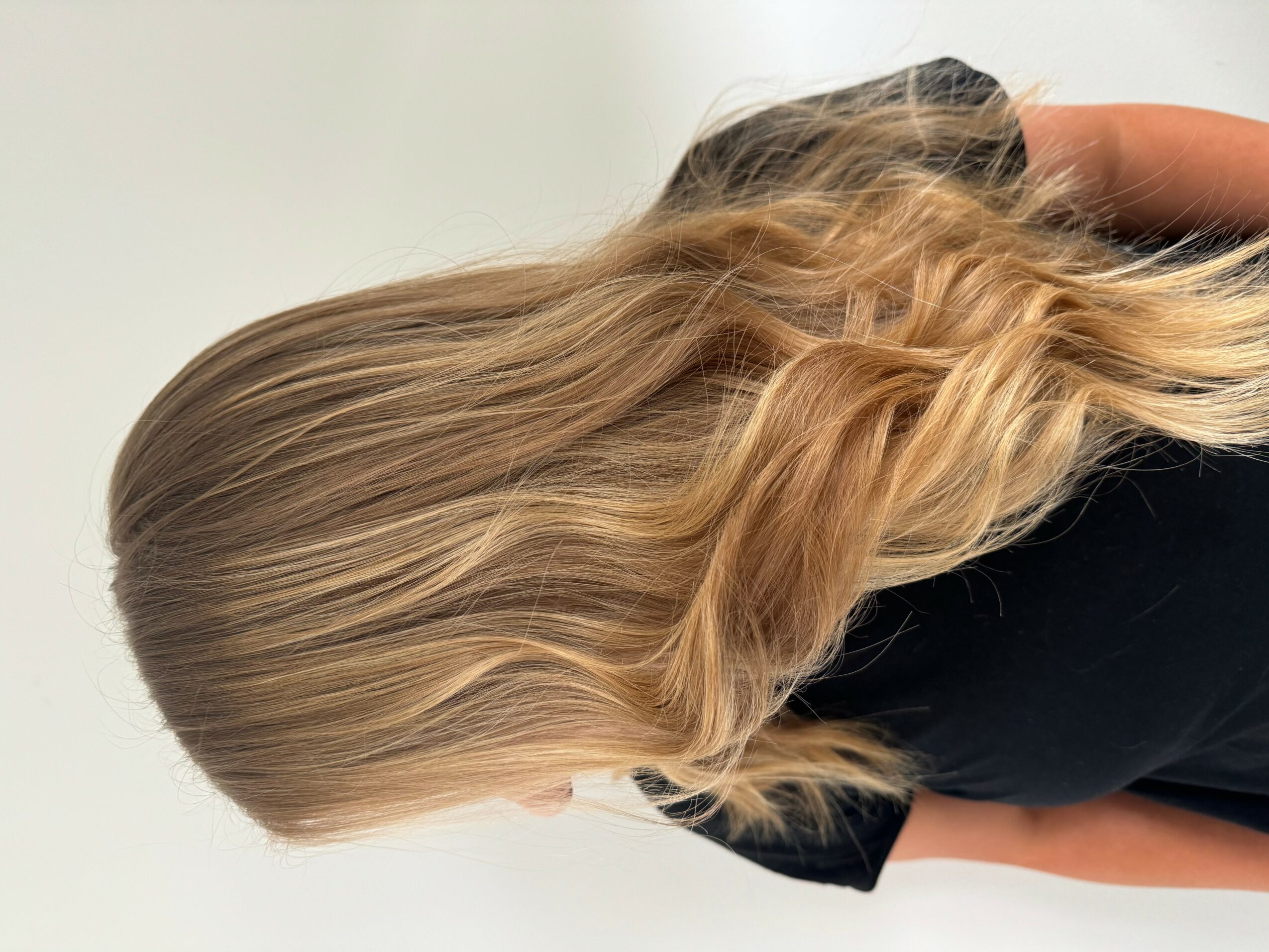 Side view of a person with long, wavy blonde hair wearing a black top.