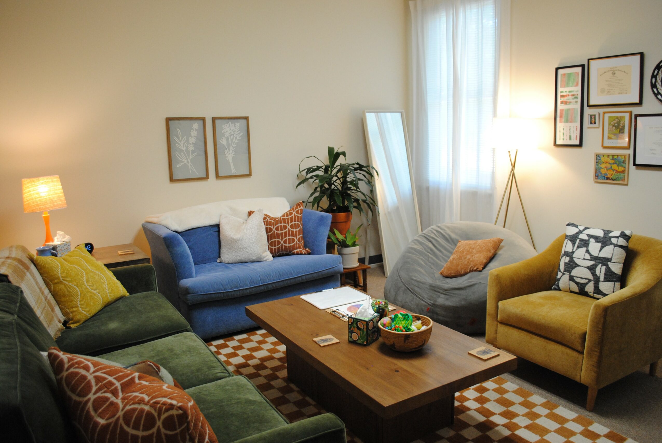 Living room with colorful sofas, a wooden coffee table, wall art, and a window with curtains.