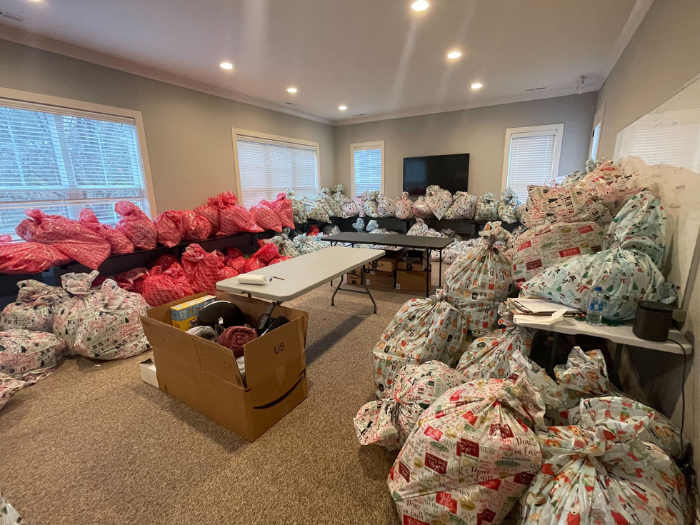 Room filled with wrapped gifts and boxes, with a table, TV, and windows, indicating a gift wrapping area.