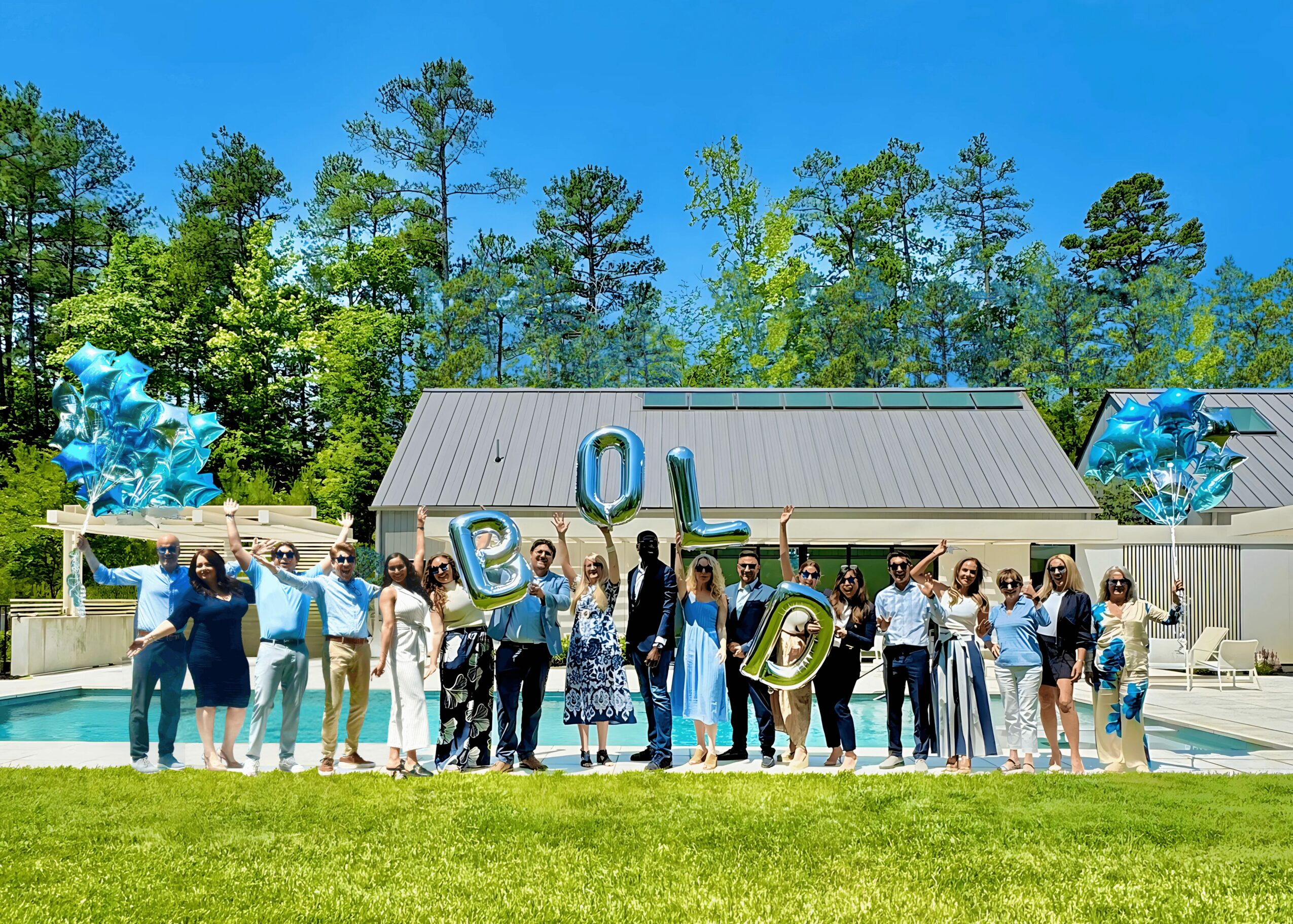 Group of people holding a large sign with letters, standing outdoors in front of a building with trees in the background.