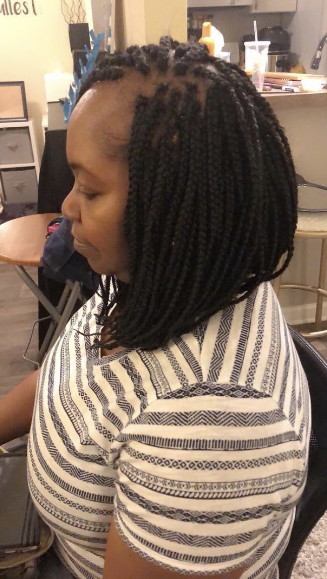 Side view of a woman with shoulder-length twisted hairstyle, wearing a striped shirt, sitting indoors.