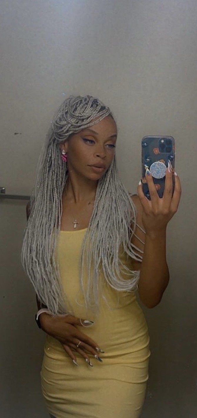 Woman with long, gray braided hair taking a mirror selfie in a yellow dress, holding a phone with a starry sky case.