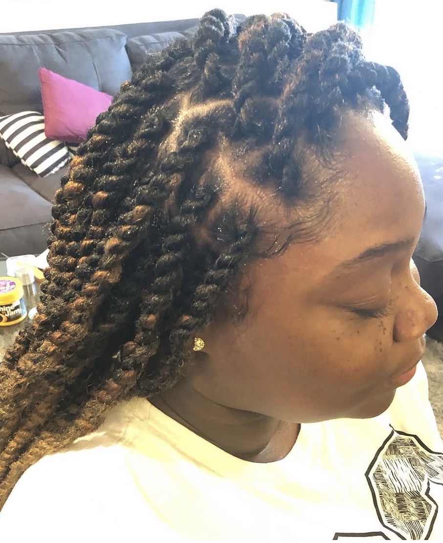 Side profile of a woman with styled dreadlocks, sitting indoors with a sofa and pillows in the background.