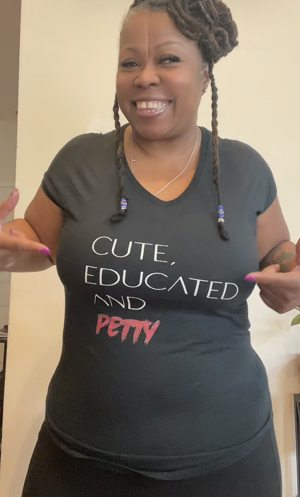 Smiling woman with braided hair pointing to her shirt that says 'CUTE, EDUCATED AND POMY'.