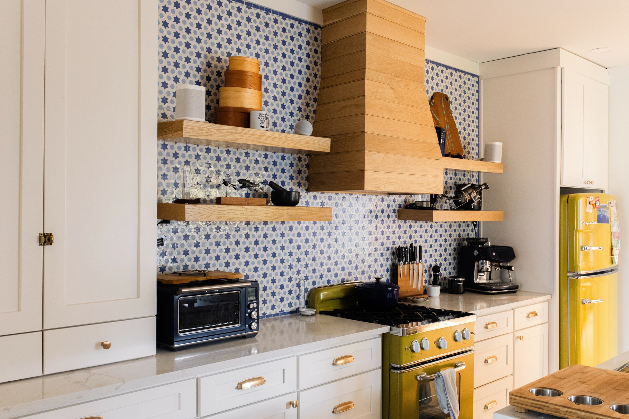 Kitchen with white cabinets, yellow refrigerator, and open wooden shelves with dishes and decor, backsplash with small blue and white tiles.