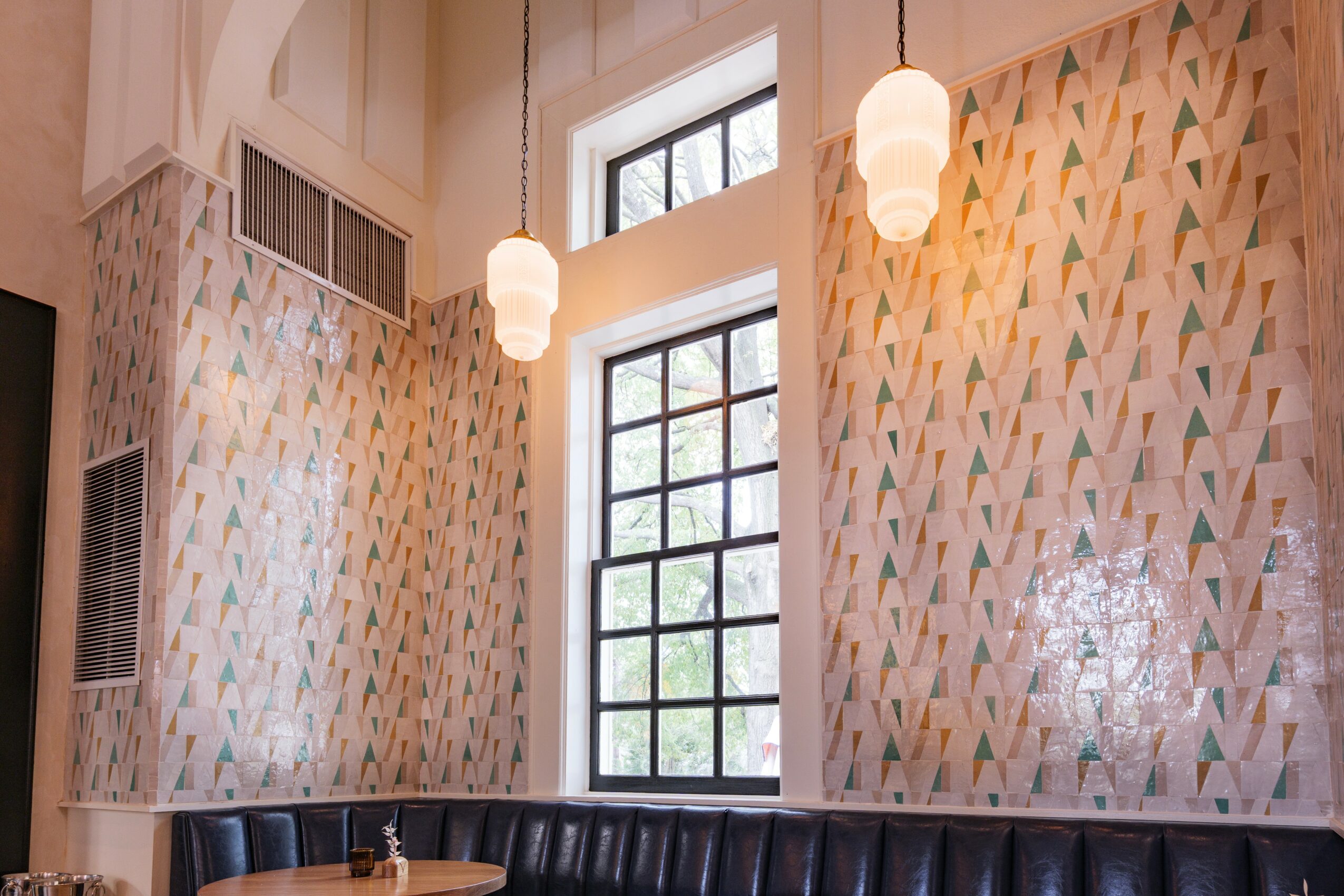 Interior room with high ceiling, large window, hanging pendant lights, patterned wallpaper, and a black sofa.