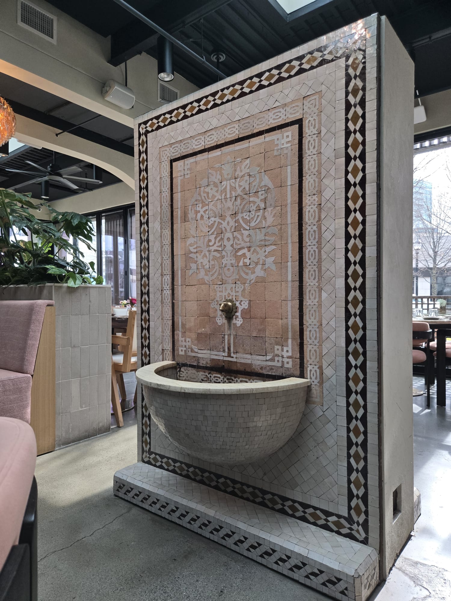 Decorative wall with a fountain, intricate tile patterns, and a basin, inside a modern interior space.