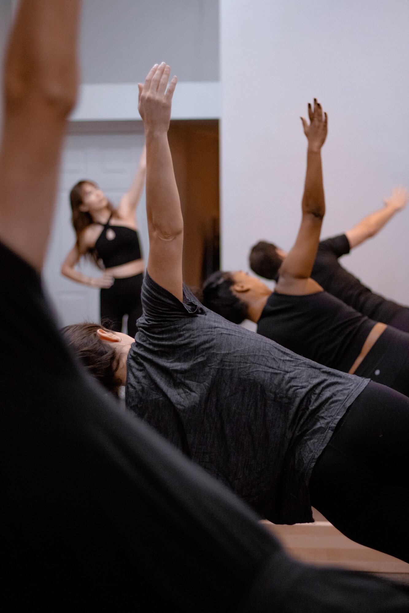 People lying on the floor with arms raised during a fitness class, focusing on a person in the foreground. Word count: 20