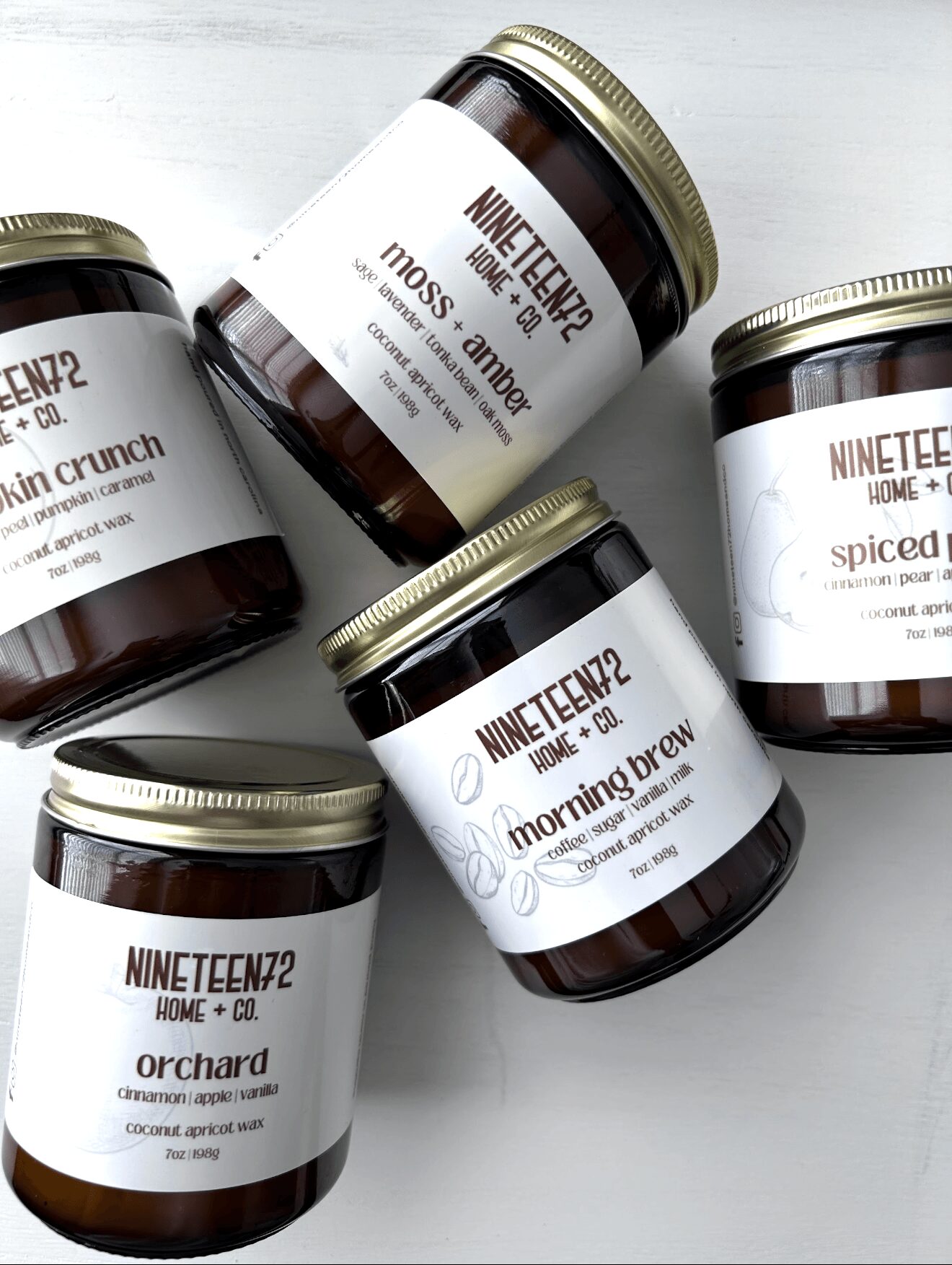 Five jars with white labels and gold lids, arranged on a white surface, containing various products.