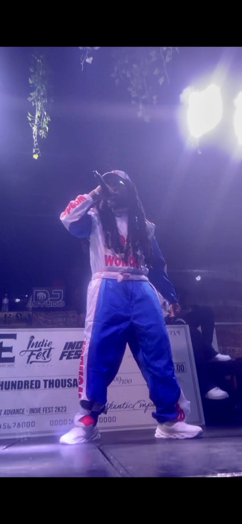 Person performing on stage with bright lights, wearing a hoodie and baggy pants, in a dance pose.