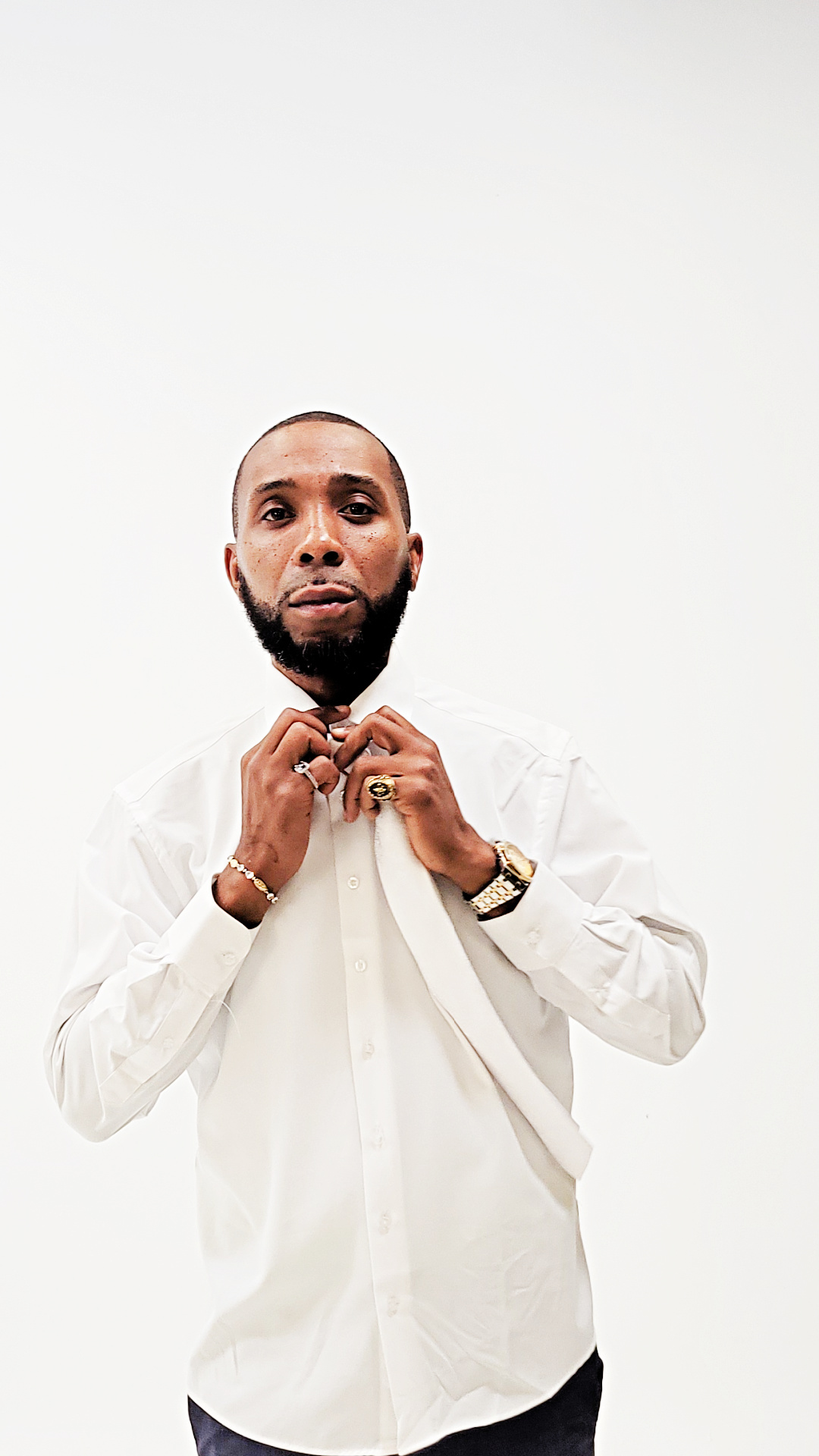 Man with a beard adjusting his white shirt collar, standing against a plain white background.