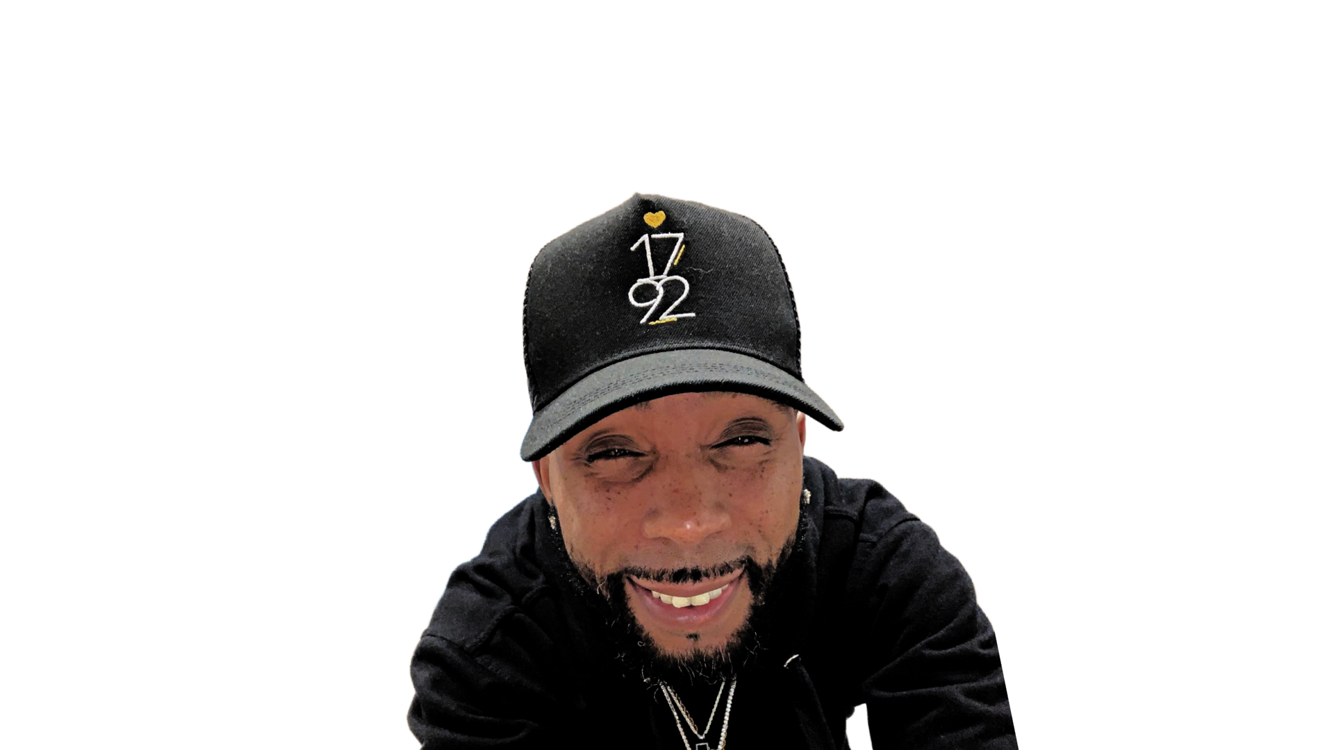 Person wearing a black cap with a logo, smiling, against a black background.