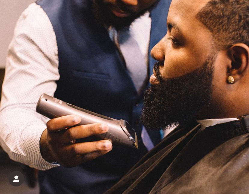 Barber using electric clipper on a man's beard, close-up of face and grooming process, in a barbershop setting.