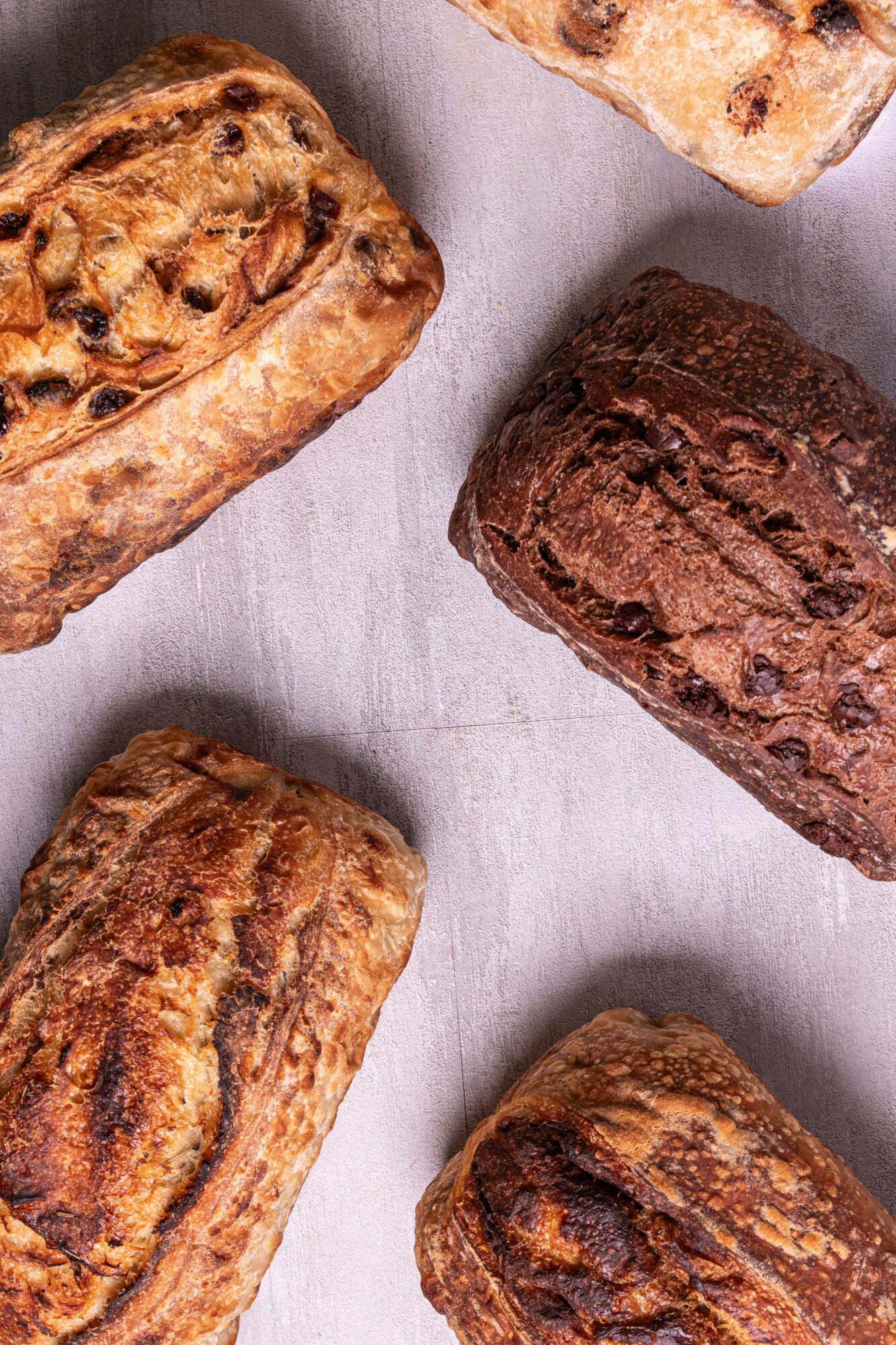 Four different types of baked bread loaves on a light surface, varying in shape and texture.