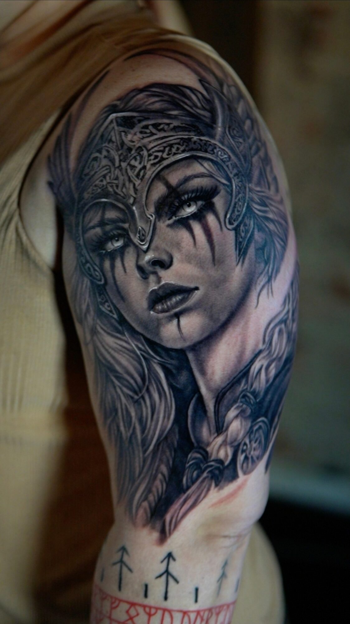 Black and gray tattoo of a woman's face with long hair and intricate designs on her forehead and around her face.