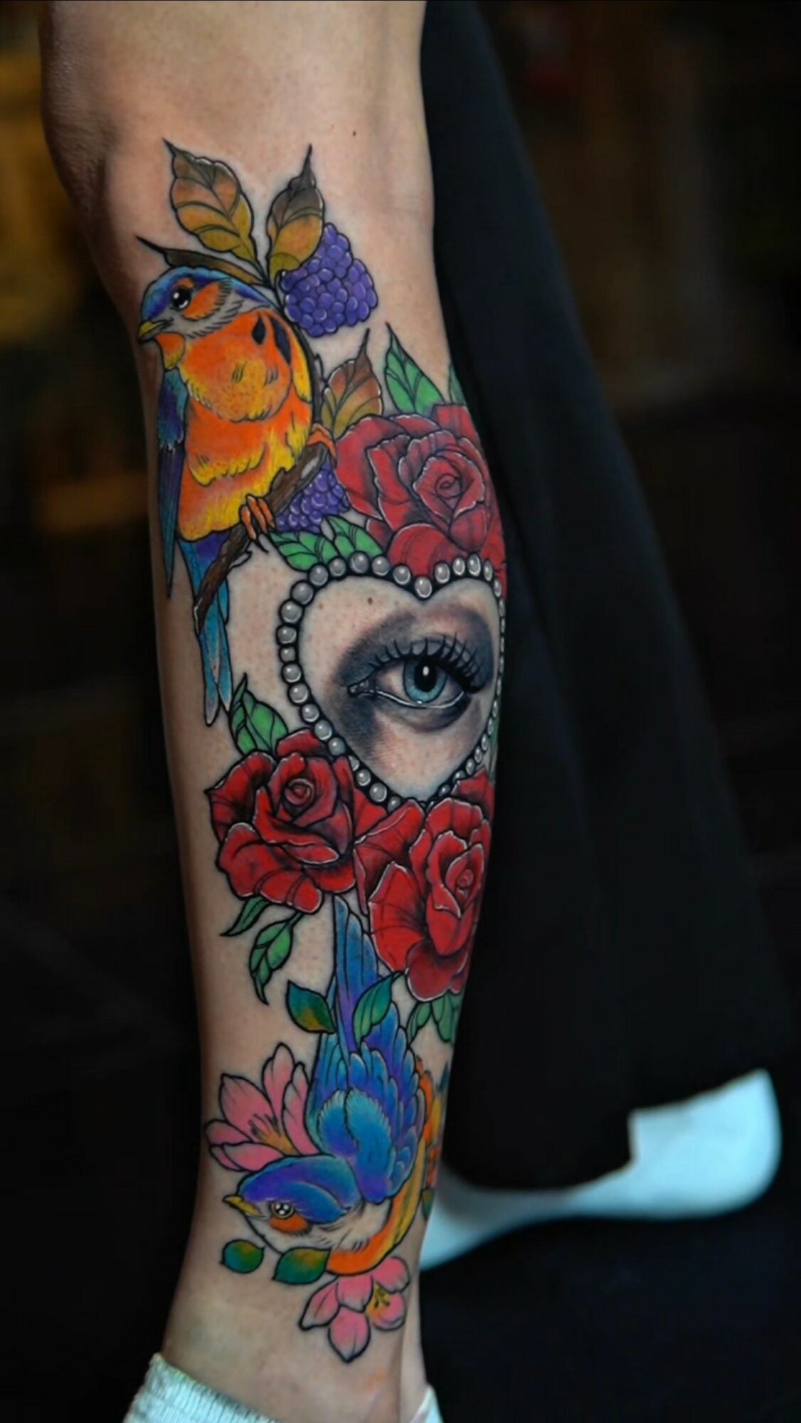 Colorful tattoo of a bird, eye, roses, and a butterfly on a person's arm.