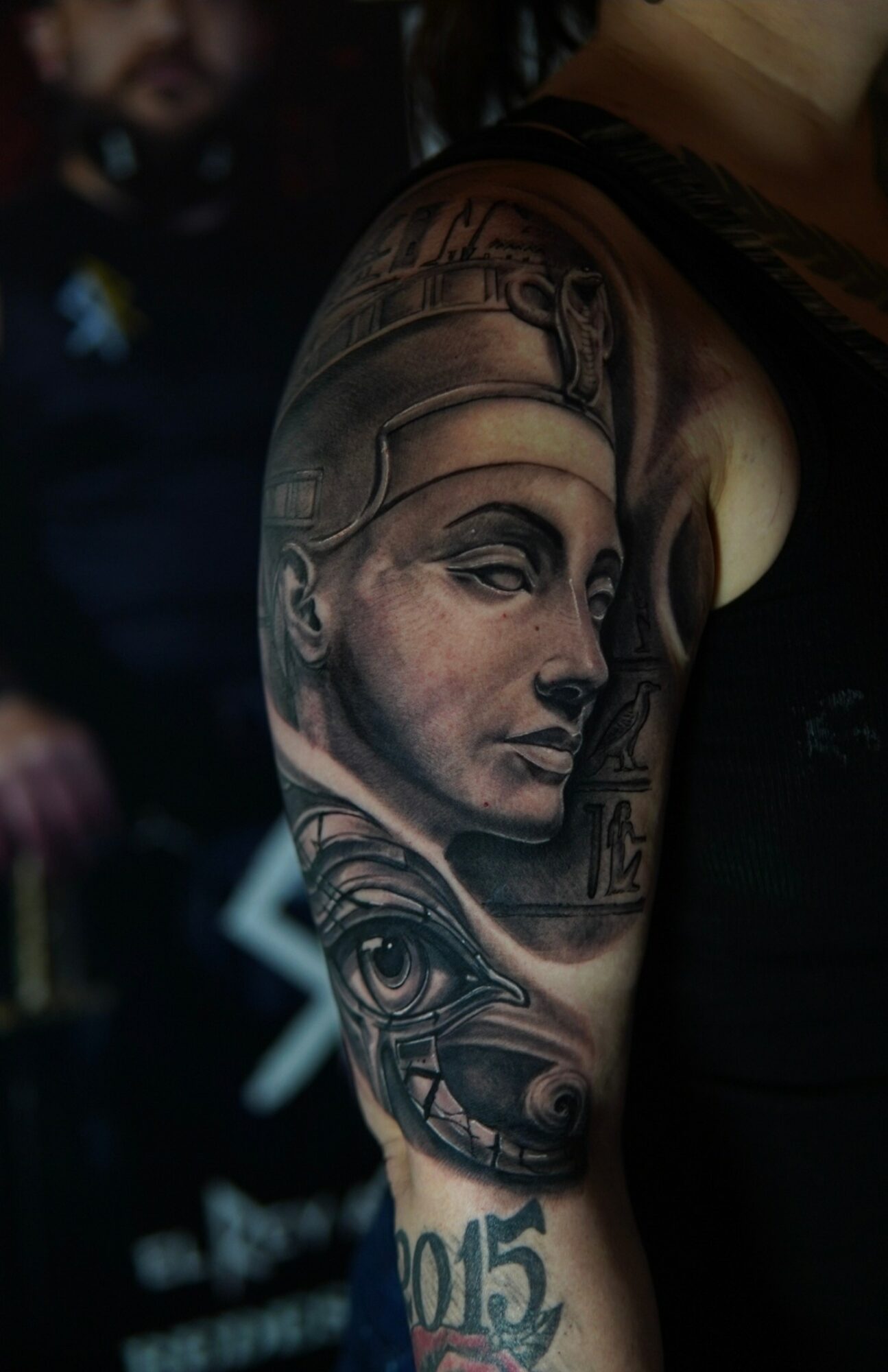 Tattoo of a woman's face with Egyptian-style headdress on person's upper arm, detailed shading and patterns.