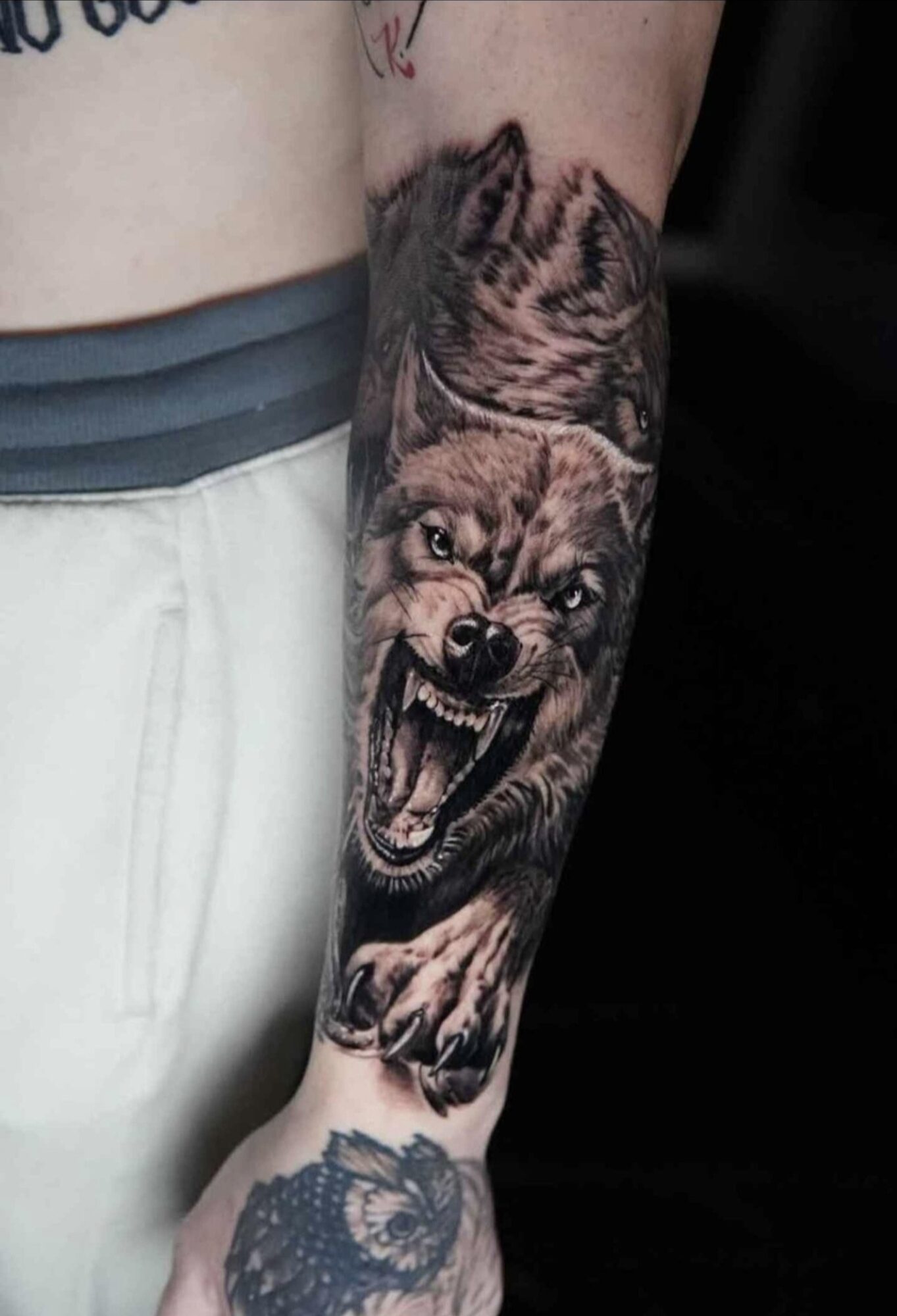 Tattoo of a snarling wolf on a person's forearm, showing detailed fur and teeth, with part of the person's clothing visible.
