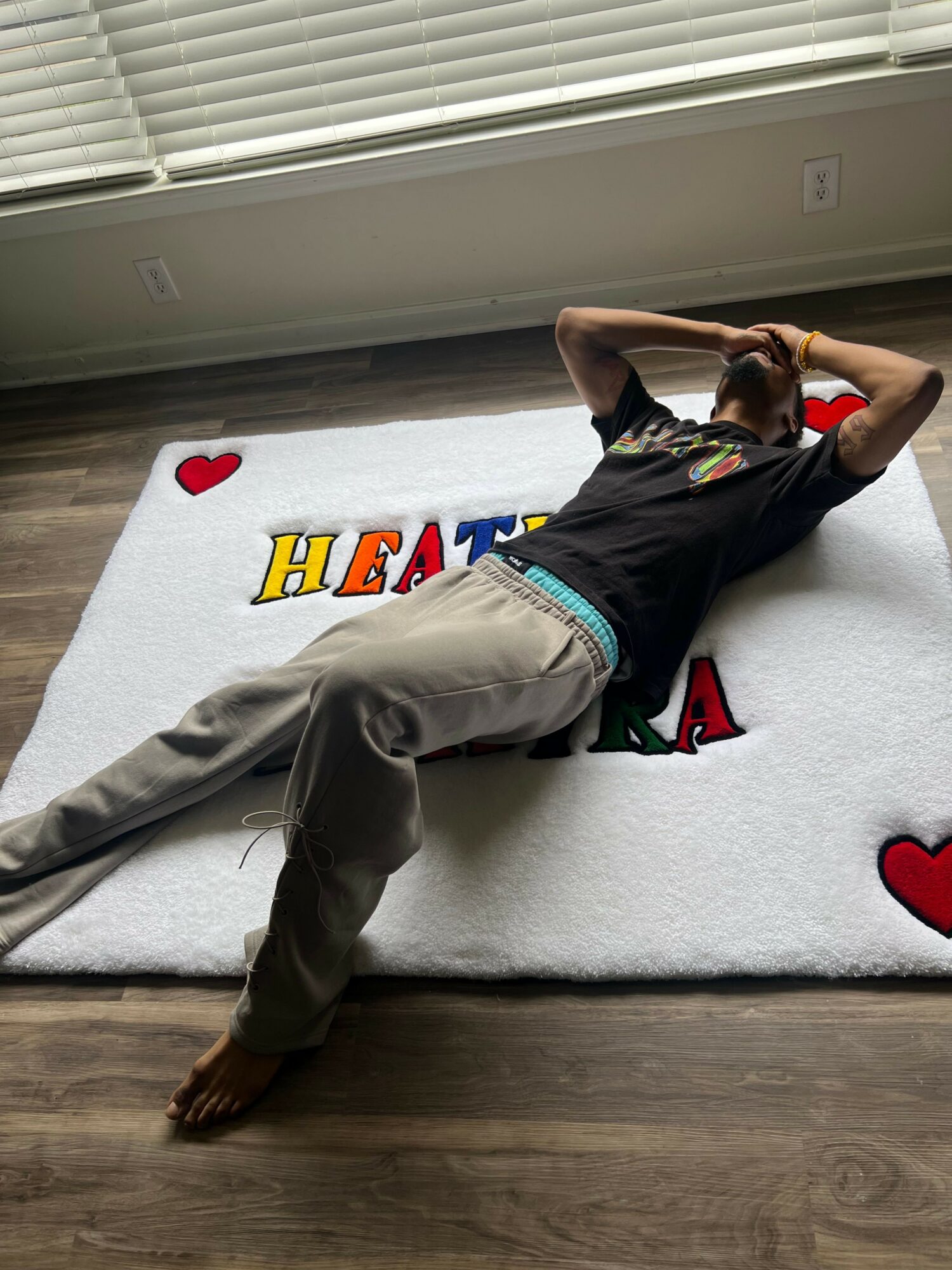 Person lying on a bed with a colorful blanket, resting their head on one arm, in a room with wooden flooring.