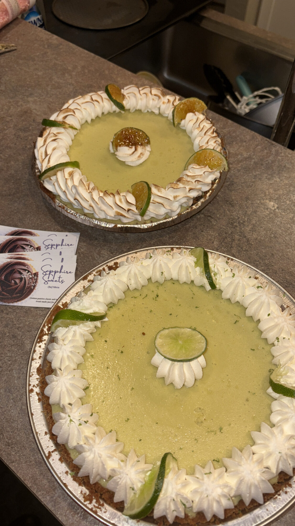 Two lime-flavored desserts with whipped cream, lime slices, and a central lime garnish on a countertop.