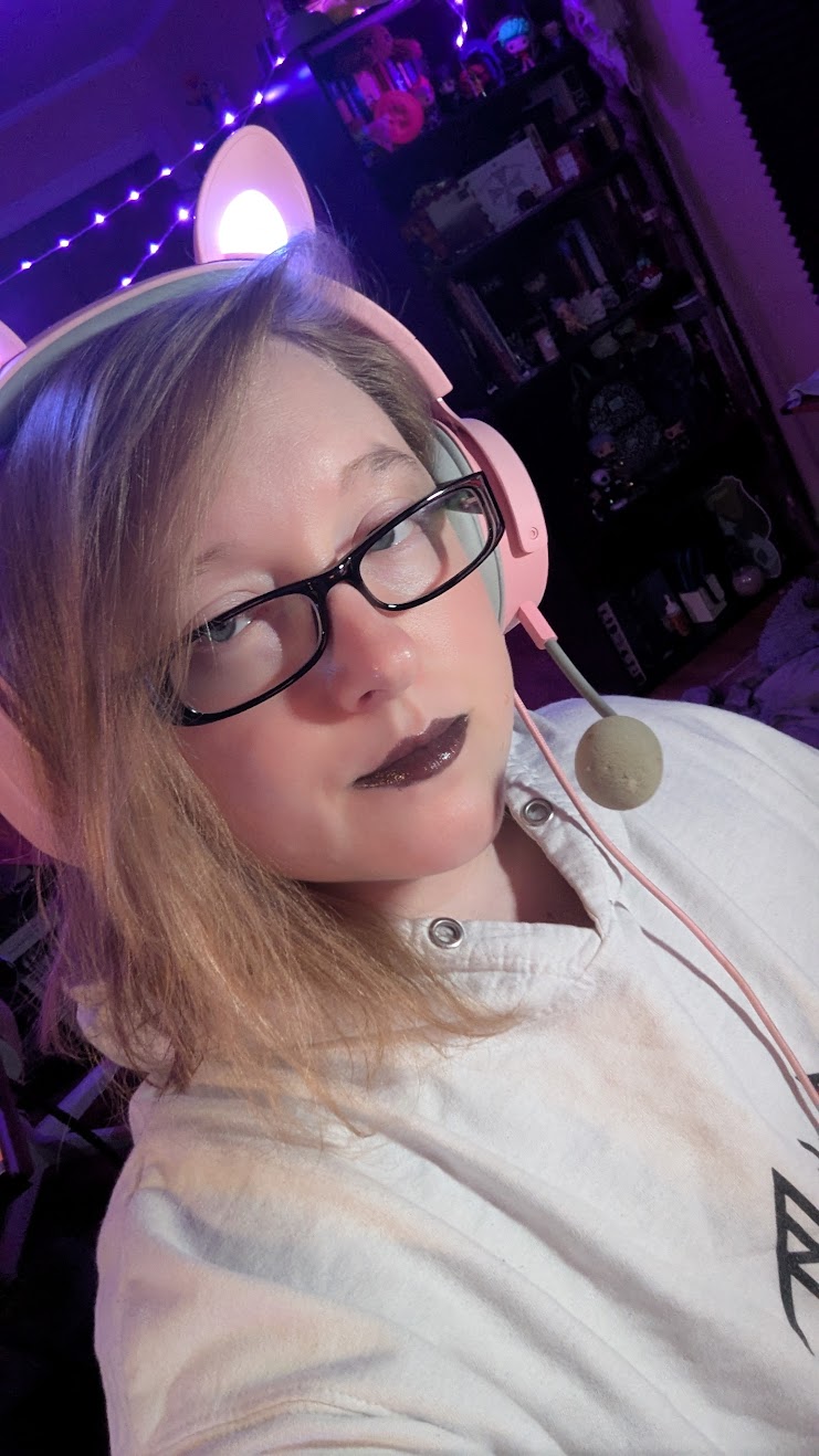 Person with glasses and dark lipstick wearing a headset, in a room with purple lighting and shelves.
