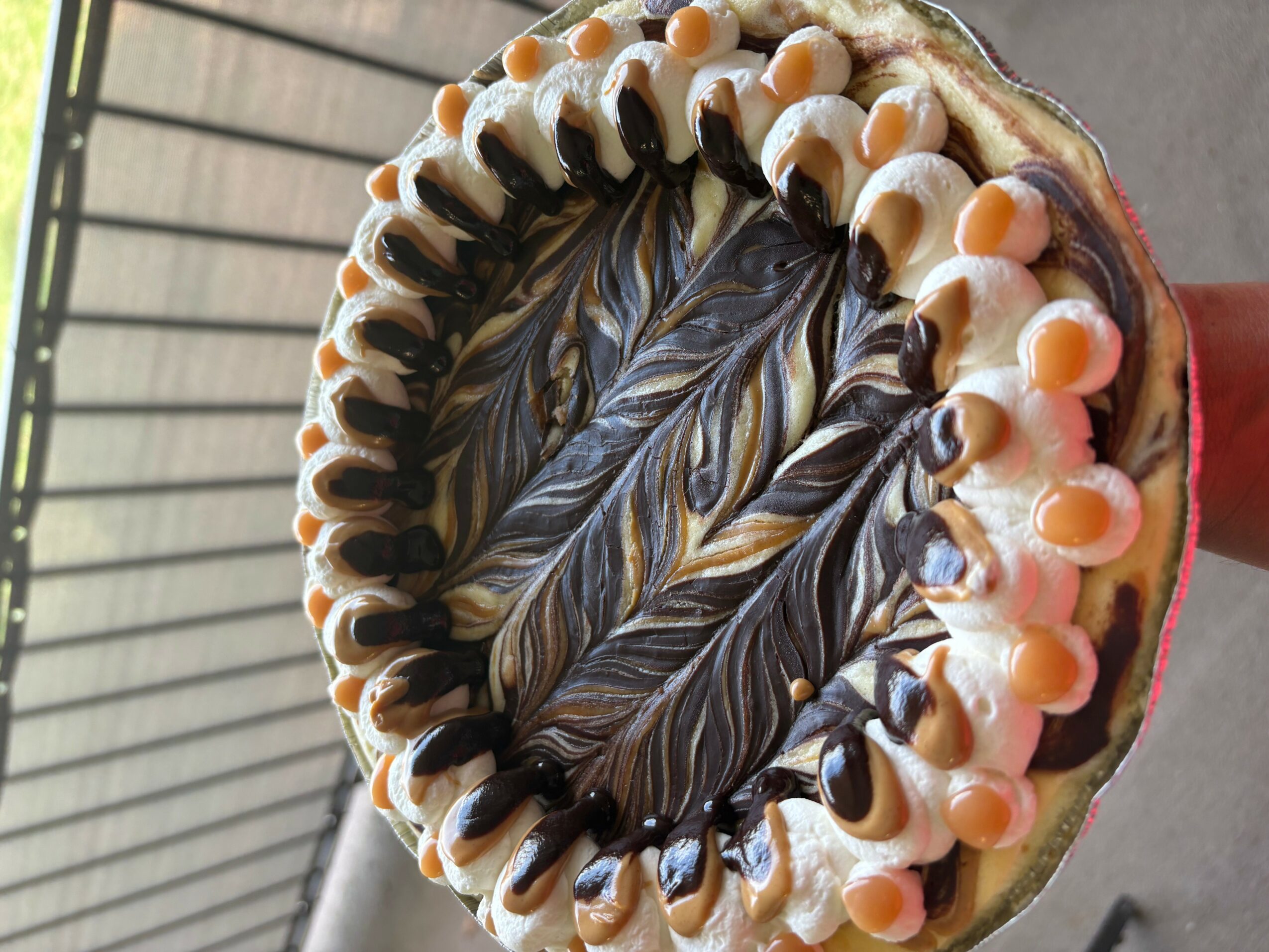 A decorated cake with swirled chocolate and vanilla frosting, topped with white and pink candies, on a gray surface.