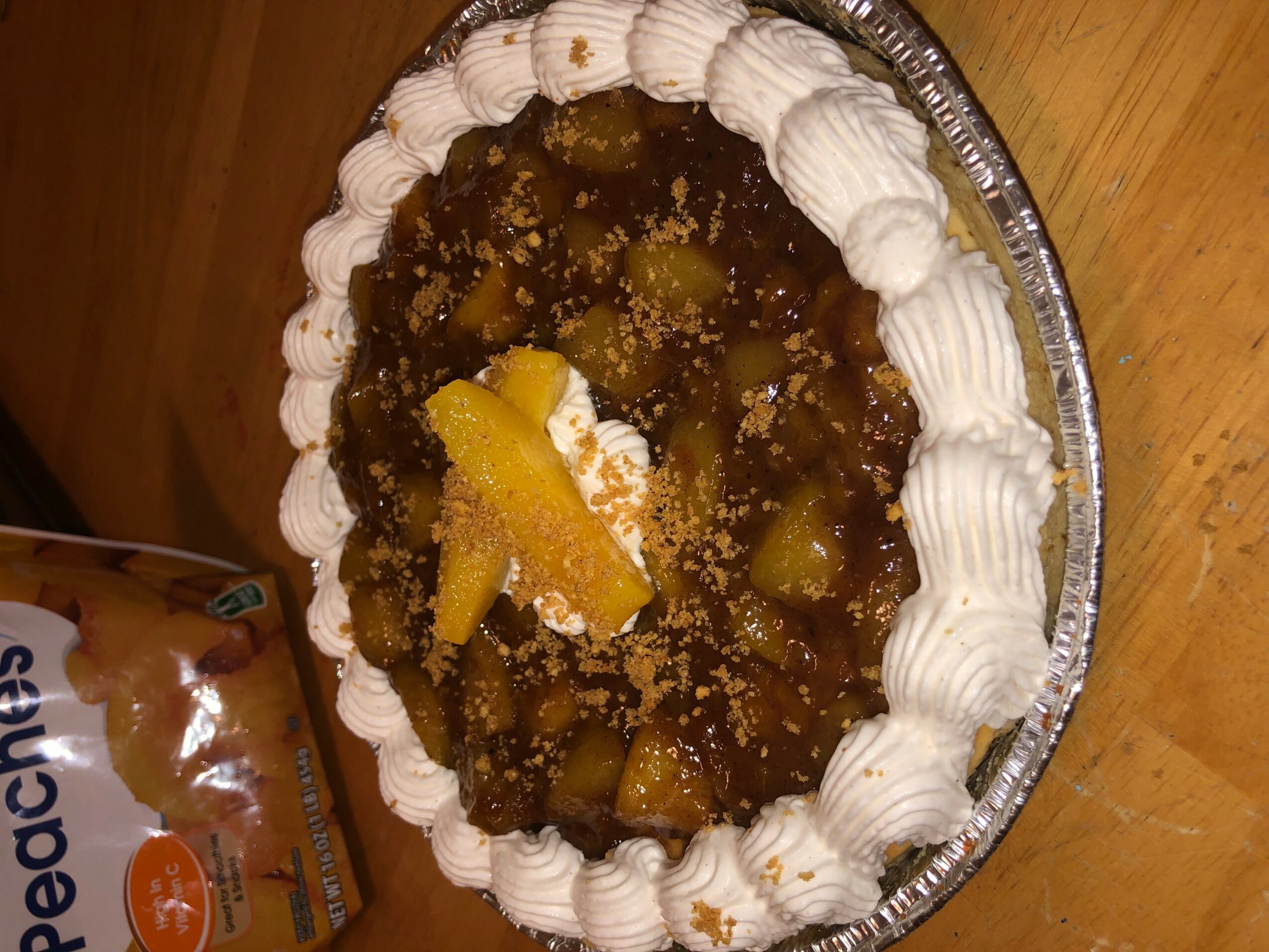 Pie with whipped cream border, topped with fruit and crumbs, on a wooden surface.