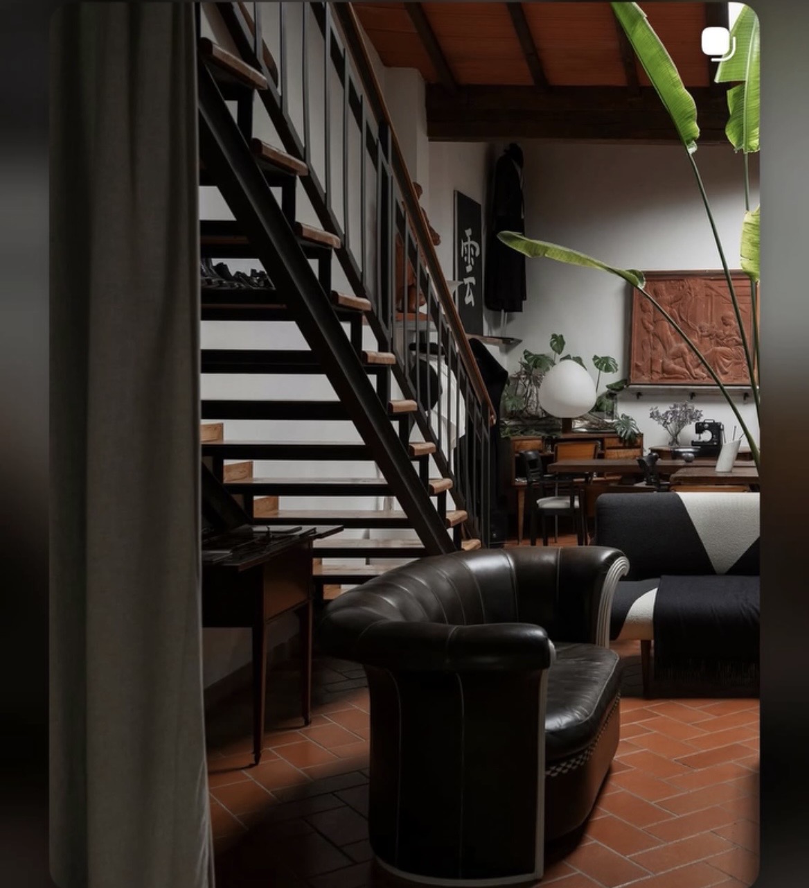 Interior of a living space with a staircase, black leather armchair, and plants, viewed from the side.