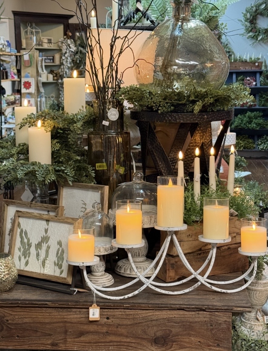 Decorative display with candles, greenery, and vases on a wooden table in a store setting.