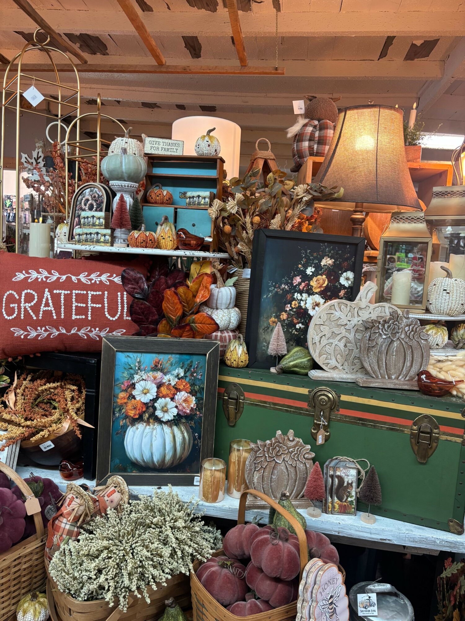 Display of decorative items including flowers, vases, and framed pictures on shelves and tables in a cozy room.