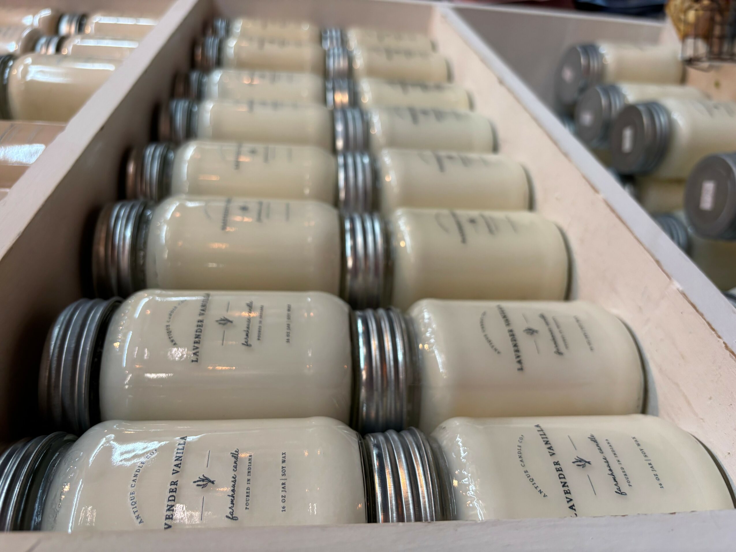 Rows of beige jars with silver lids on a shelf, with additional jars in the background.
