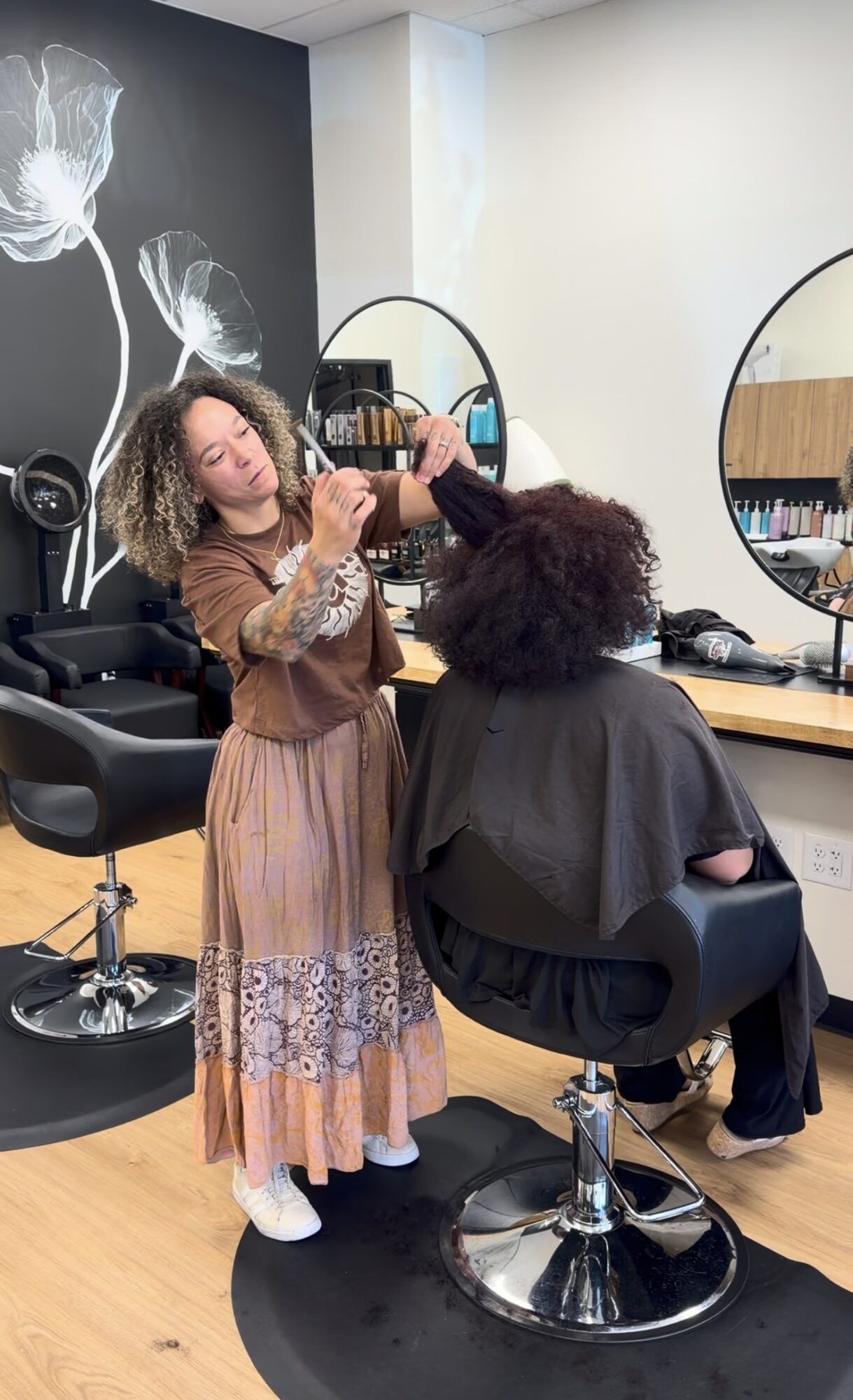 A woman with curly hair is getting her hair styled by a hairstylist in a salon. The salon has mirrors and hair products.